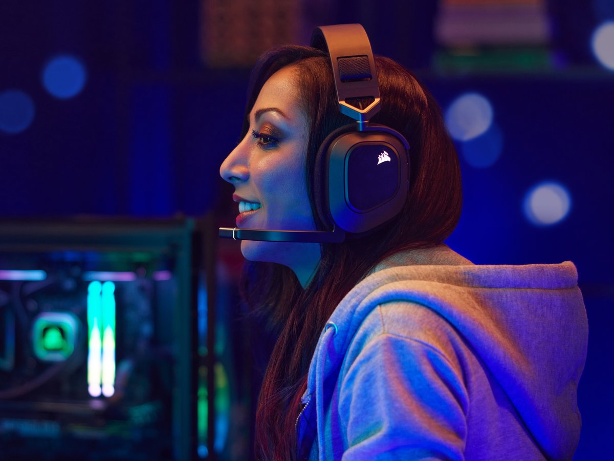 Eine Frau in einem grauen Kapuzenpullover trägt ein Gaming-Headset, lächelnd.