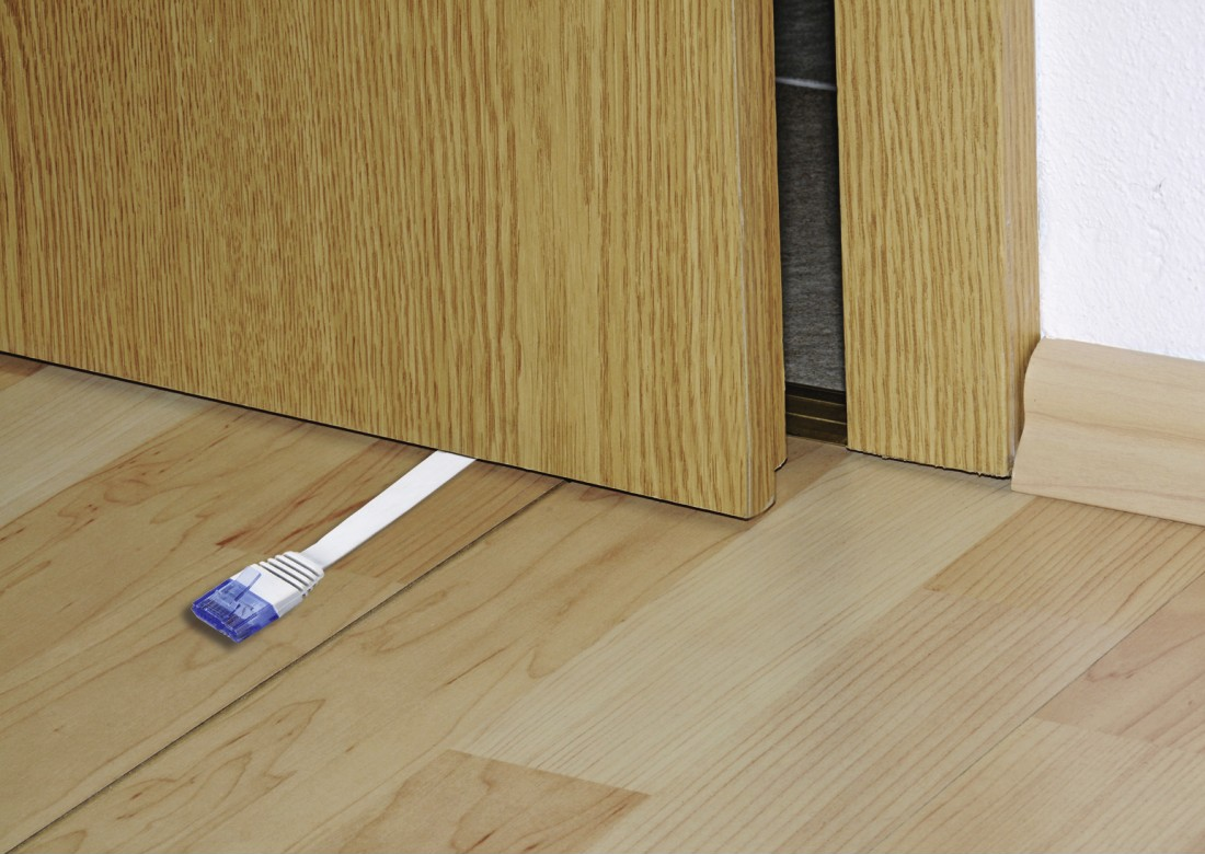 Un cavo Ethernet bianco esce da sotto una porta di legno. Il pavimento è in legno chiaro. Il muro è bianco.