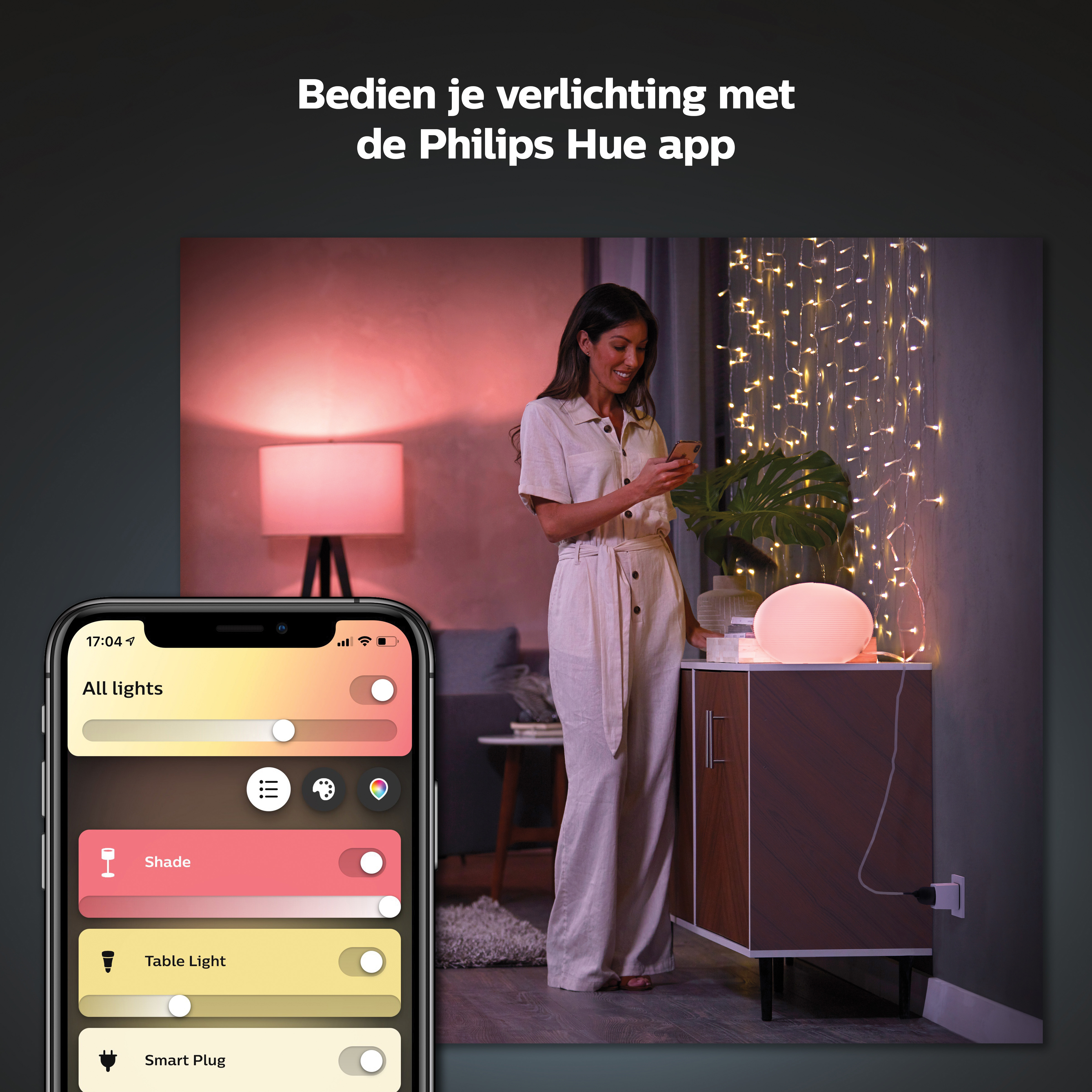 A woman is using her phone to control smart home lighting. A lamp and fairy lights are on.