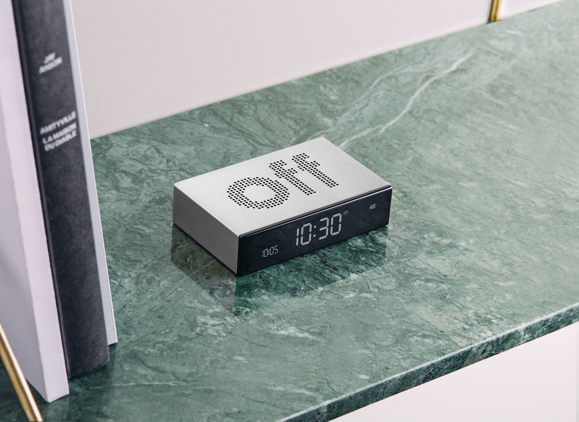 Sveglia argentata con display spento. È su una superficie di marmo verde con libri.