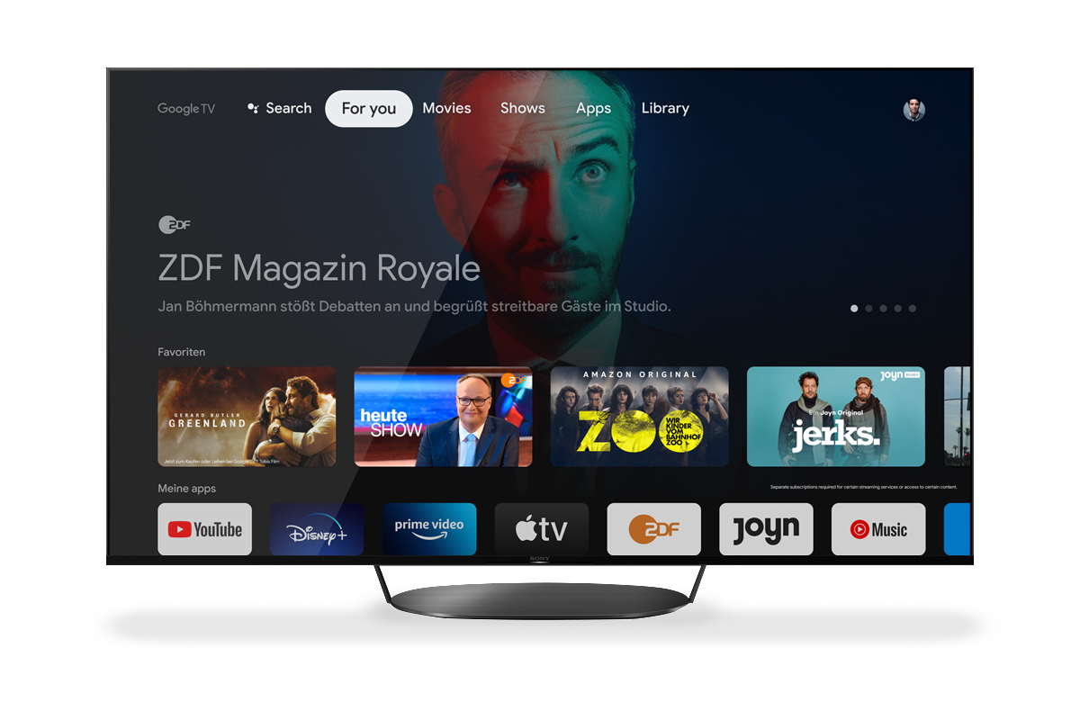 Ein Smart-TV-Bildschirm mit Google TV-Oberfläche, der verschiedene Streaming-App-Symbole und ein Gesicht zeigt.