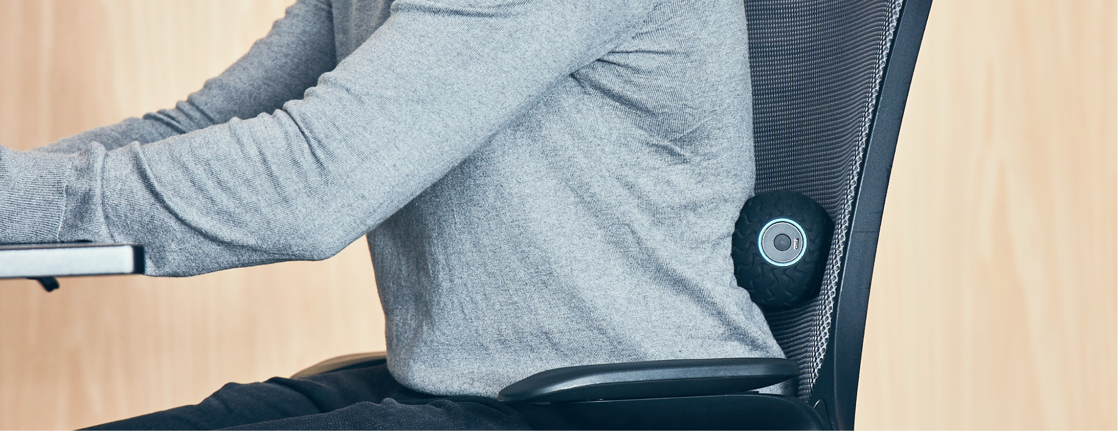 Person sitzt in einem Stuhl mit einem schwarzen Massagegerät am unteren Rücken. Sie arbeiten.