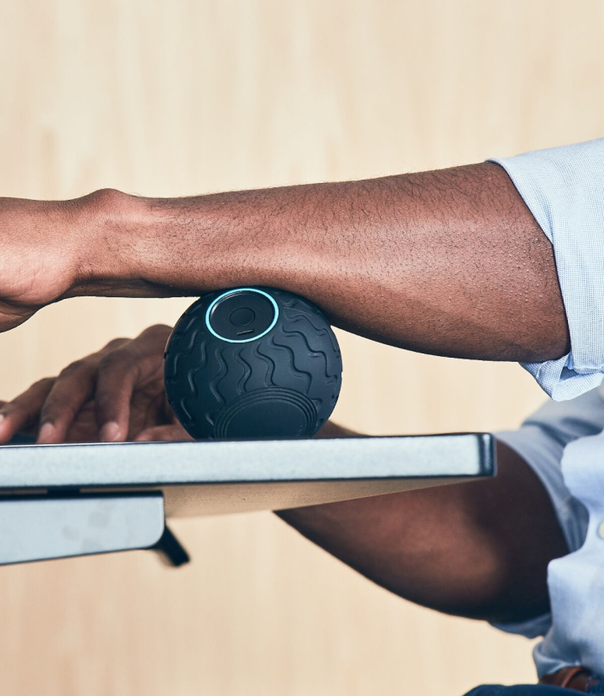 Ein Arm ruht auf einem Schreibtisch und rollt einen schwarzen Massageball.