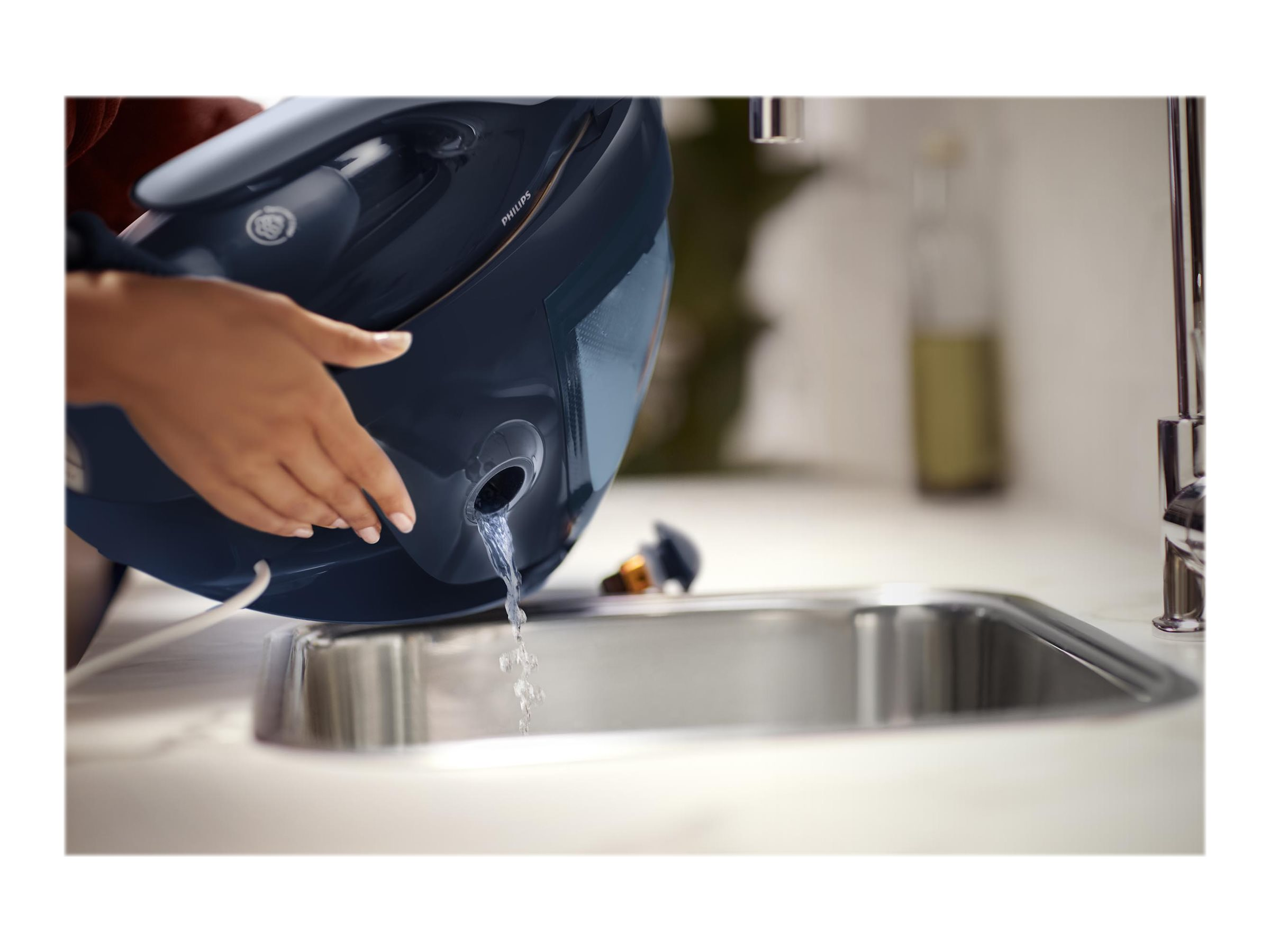 Hände, die ein Waschbecken mit Wasser aus einem dunkelblauen Bügeleisen füllen.