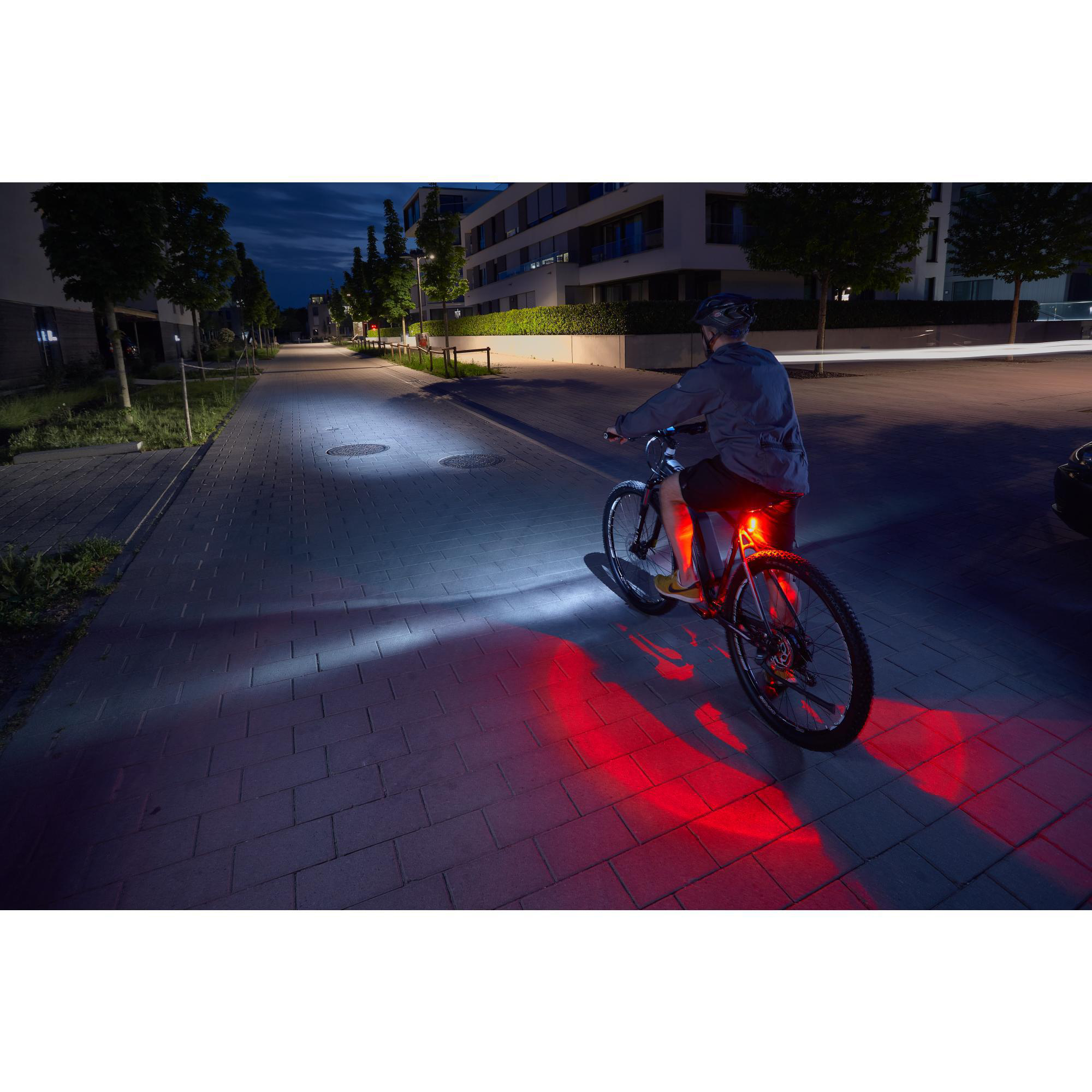 Ein Radfahrer fährt nachts auf einer Straße. Rote Rücklichter, weiße Frontlichter.