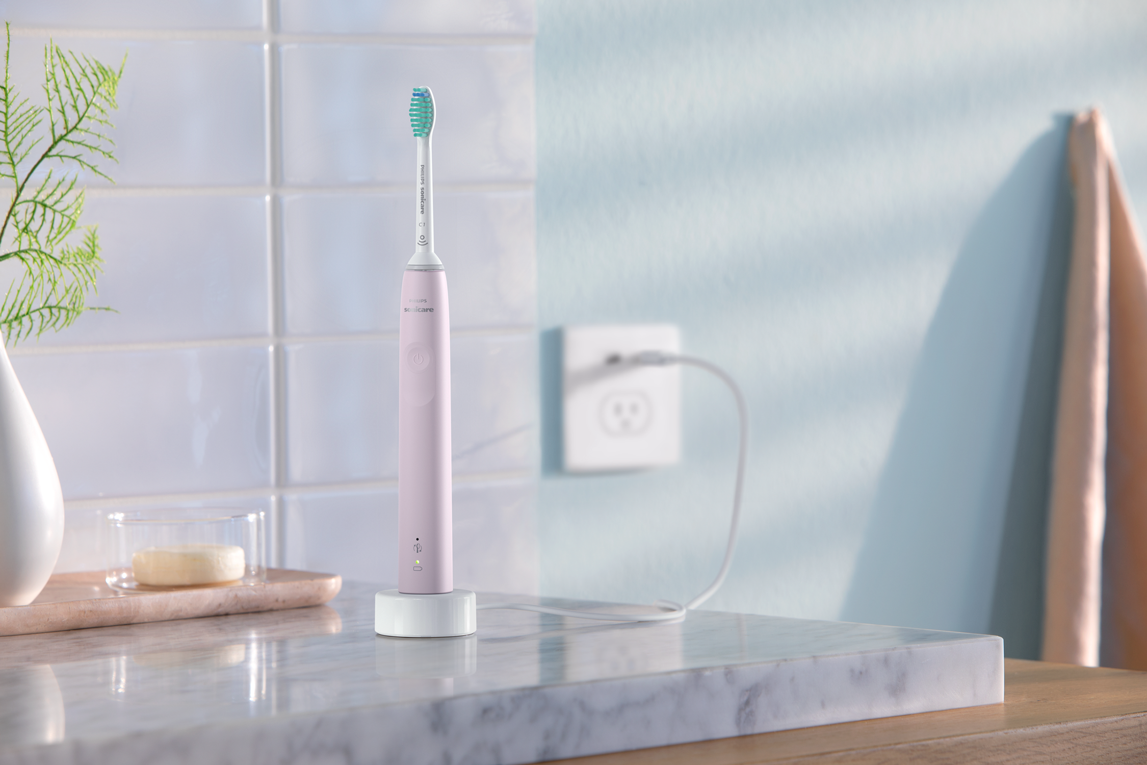 Roze elektrische tandenborstel op oplader, witte muur, glas en marmer. Licht van raam.