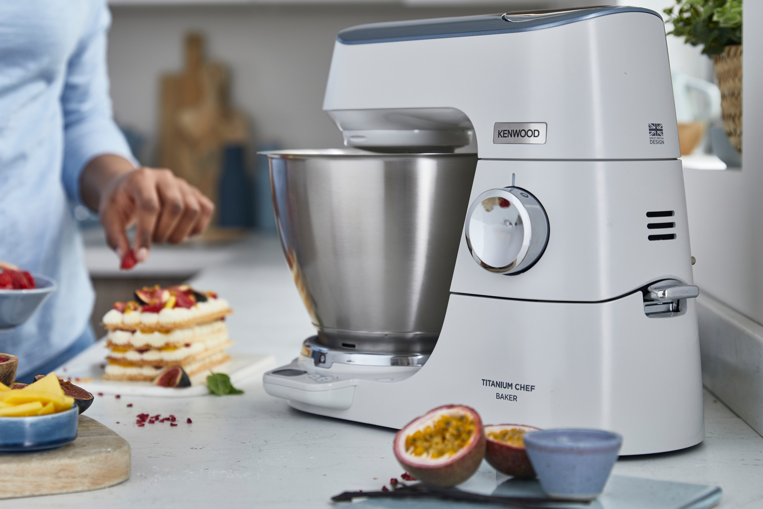 Kenwood Titanium Chef Baker, mit einer Person, die Früchte hinzufügt, auf einer Küchenarbeitsplatte.