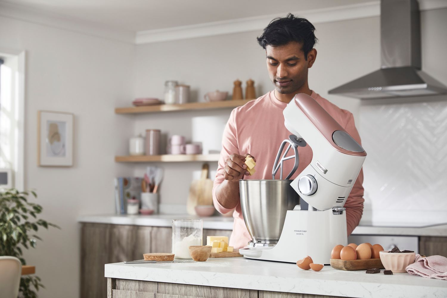 Ein Mann fügt Butter in einen Mixer hinzu, Mehl, Eier und Schokolade sind in der Nähe.