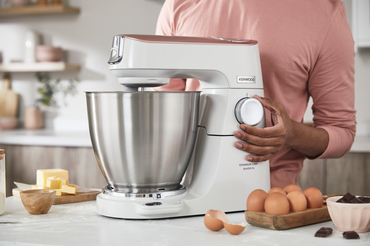 Eine Frau mit einem Kenwood-Mixer in einer Küche, Zutaten in der Nähe.