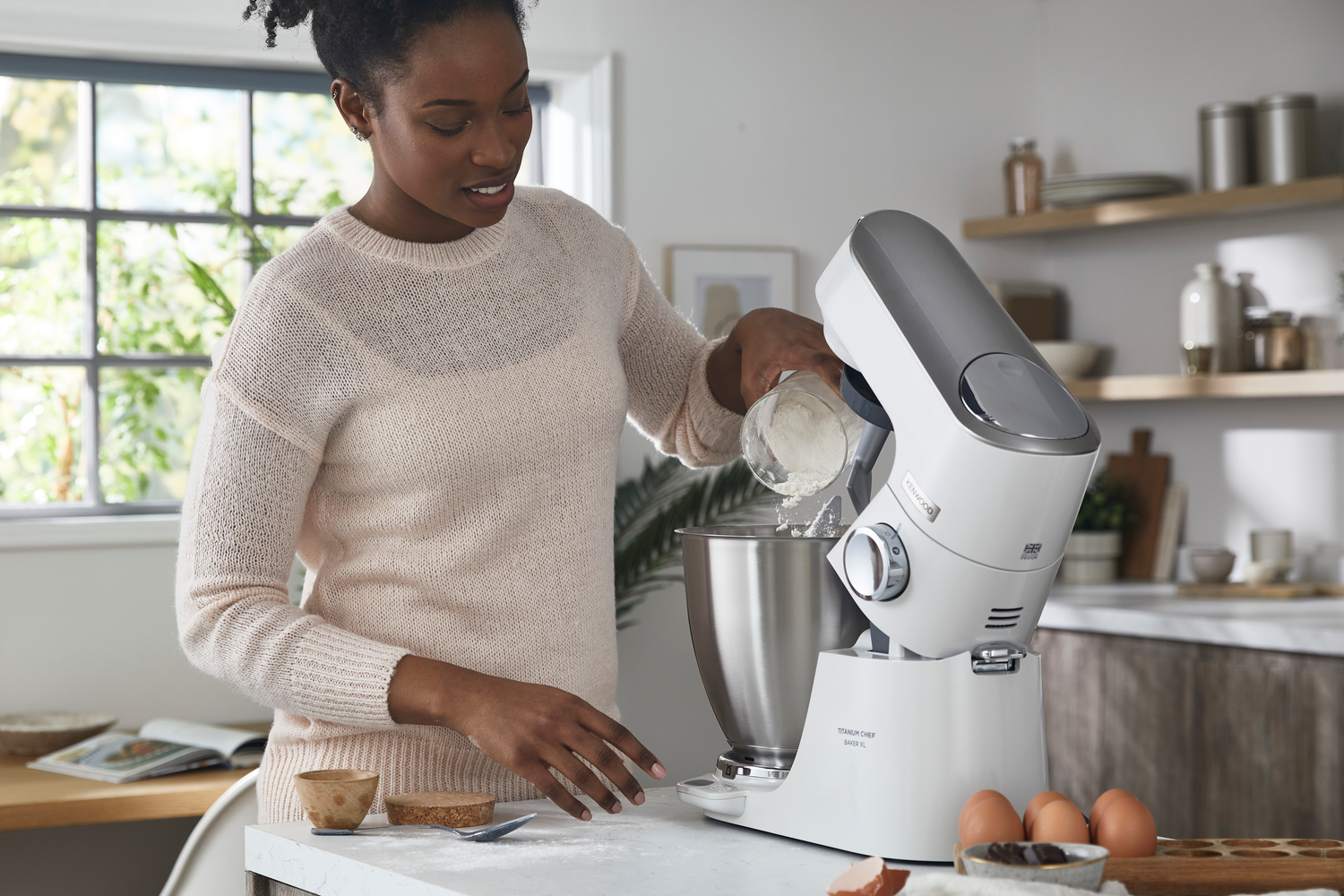 Frau, die Mehl in einen weißen KitchenAid-Küchenmixer gießt.