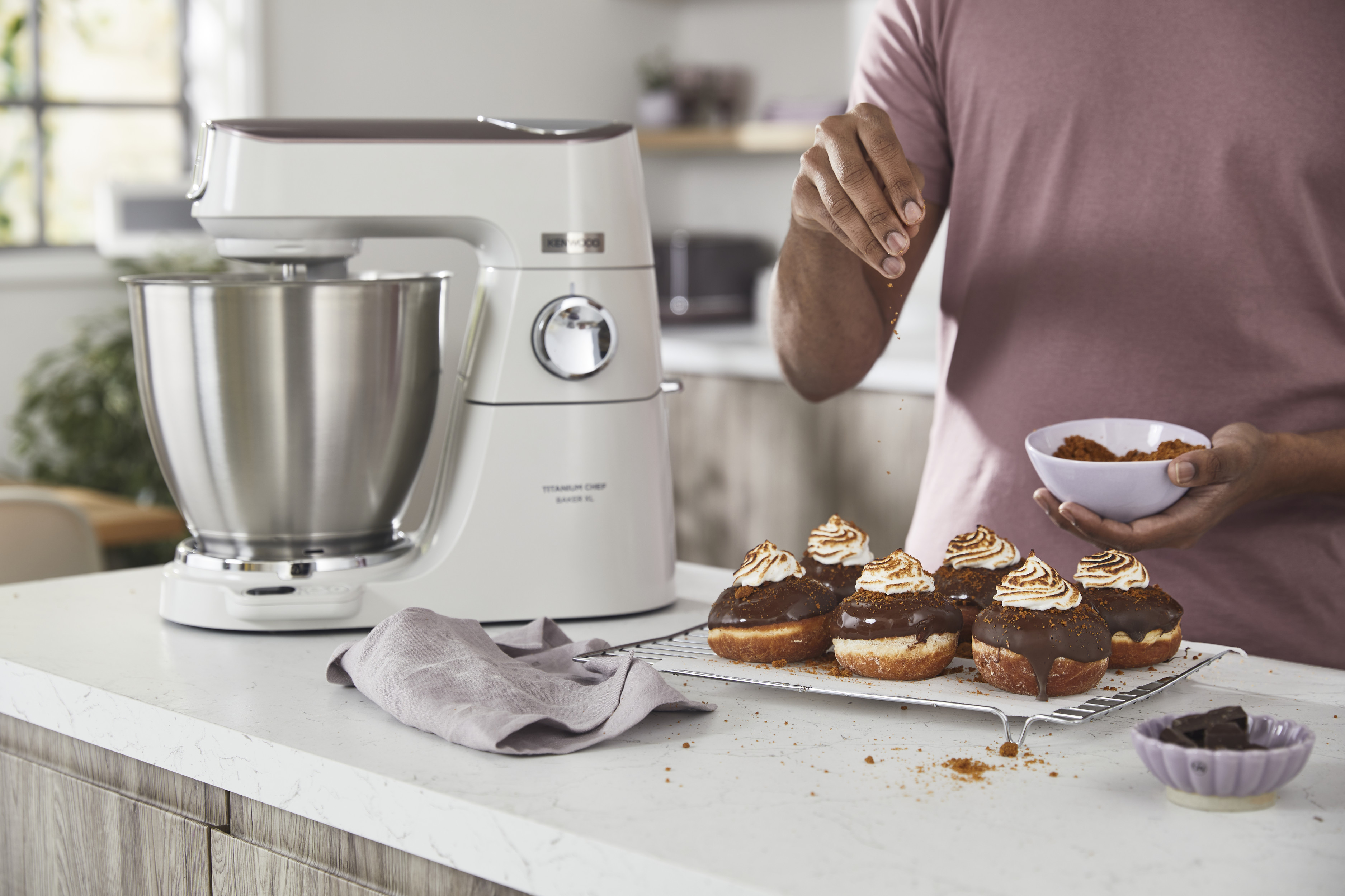 Eine Person streut Toppings auf Donuts. Ein Küchenmixer ist im Hintergrund.
