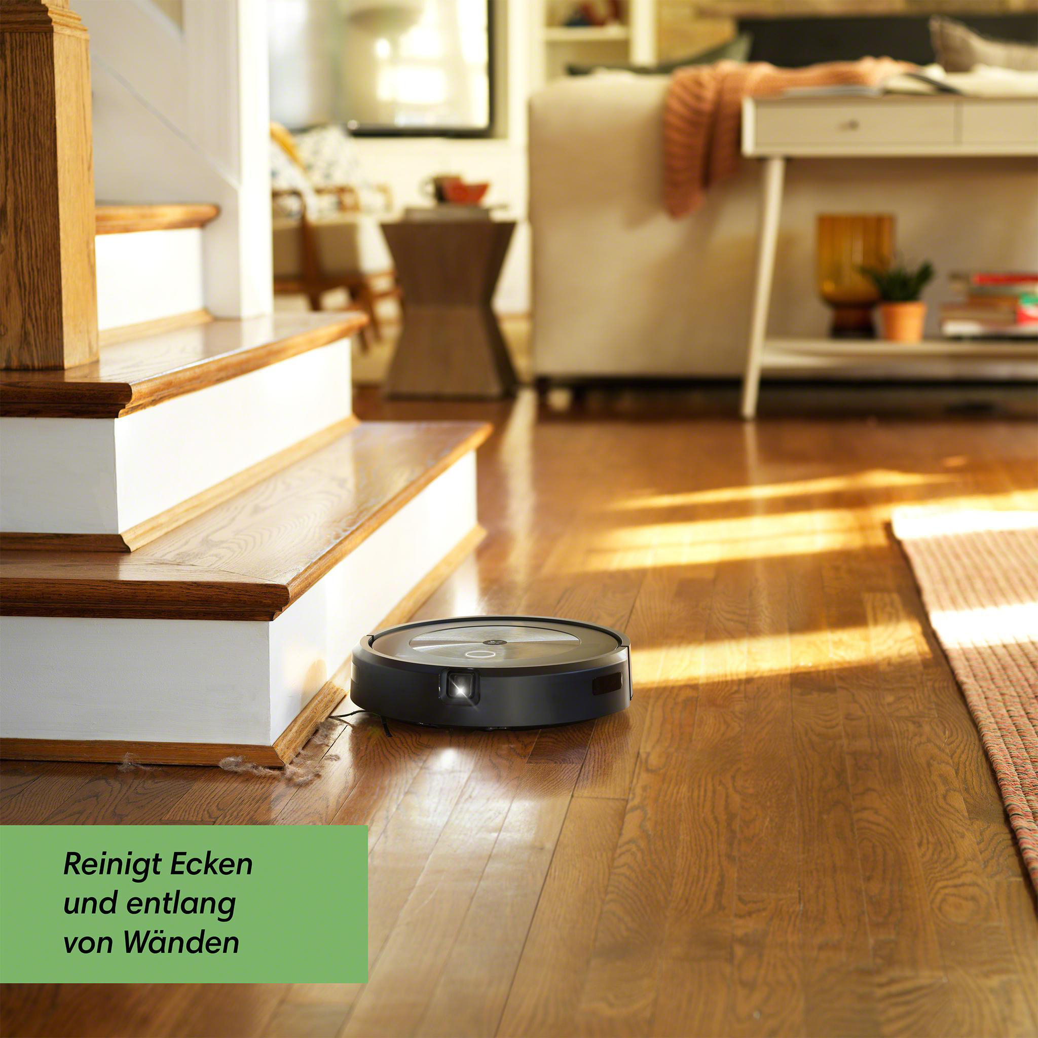 Ein schwarzer Roboter-Staubsauger auf Holzboden, in der Nähe einer Treppe.