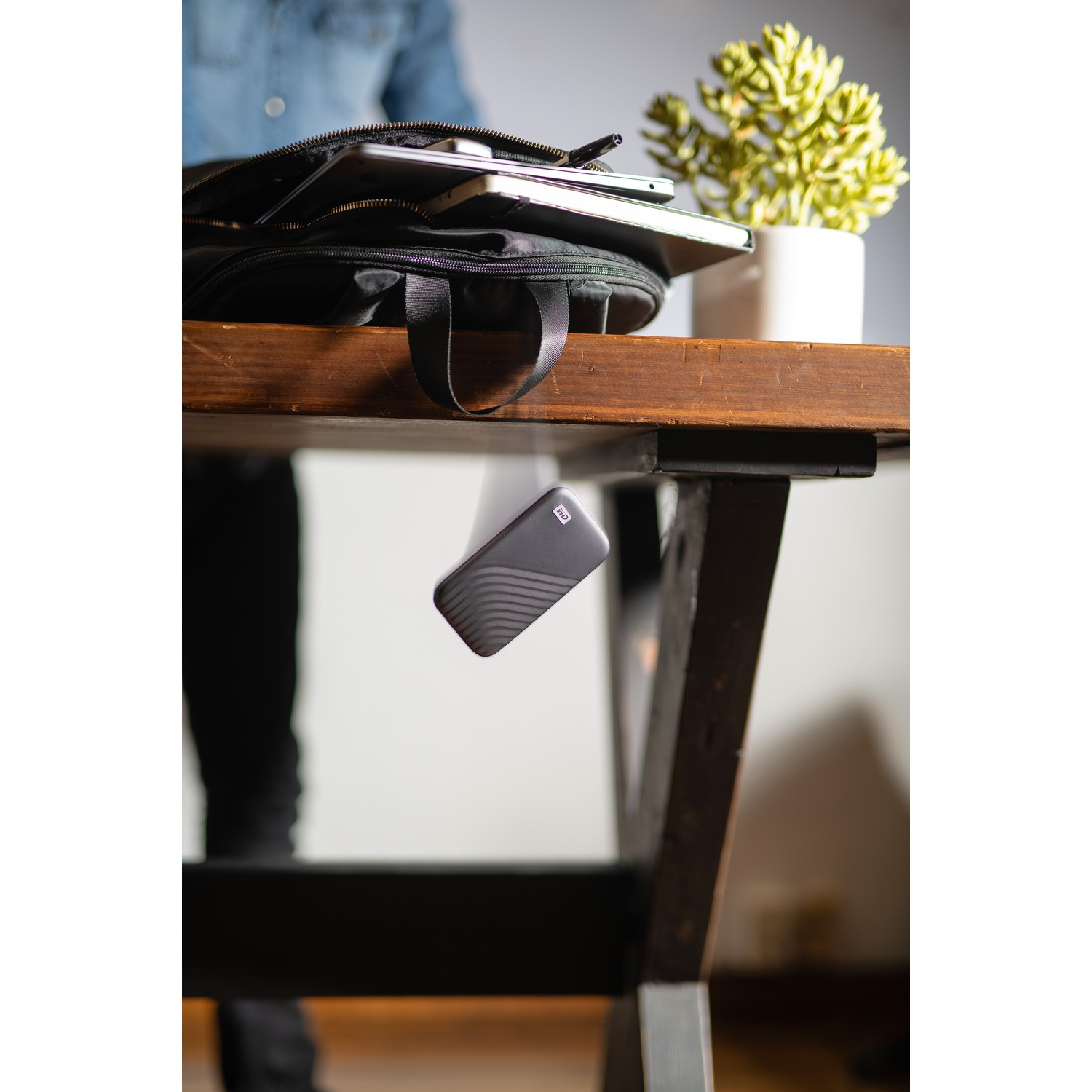 Un disco duro cae cerca de una mesa. Una persona está en el fondo. Hay una planta en la mesa.