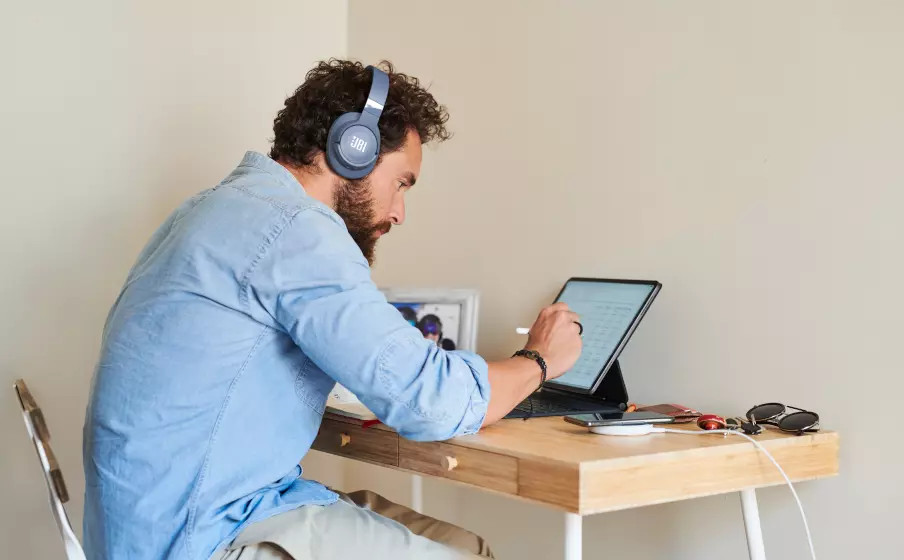 Homme barbu portant un casque bleu, travaillant sur une tablette avec un stylo, à un bureau.