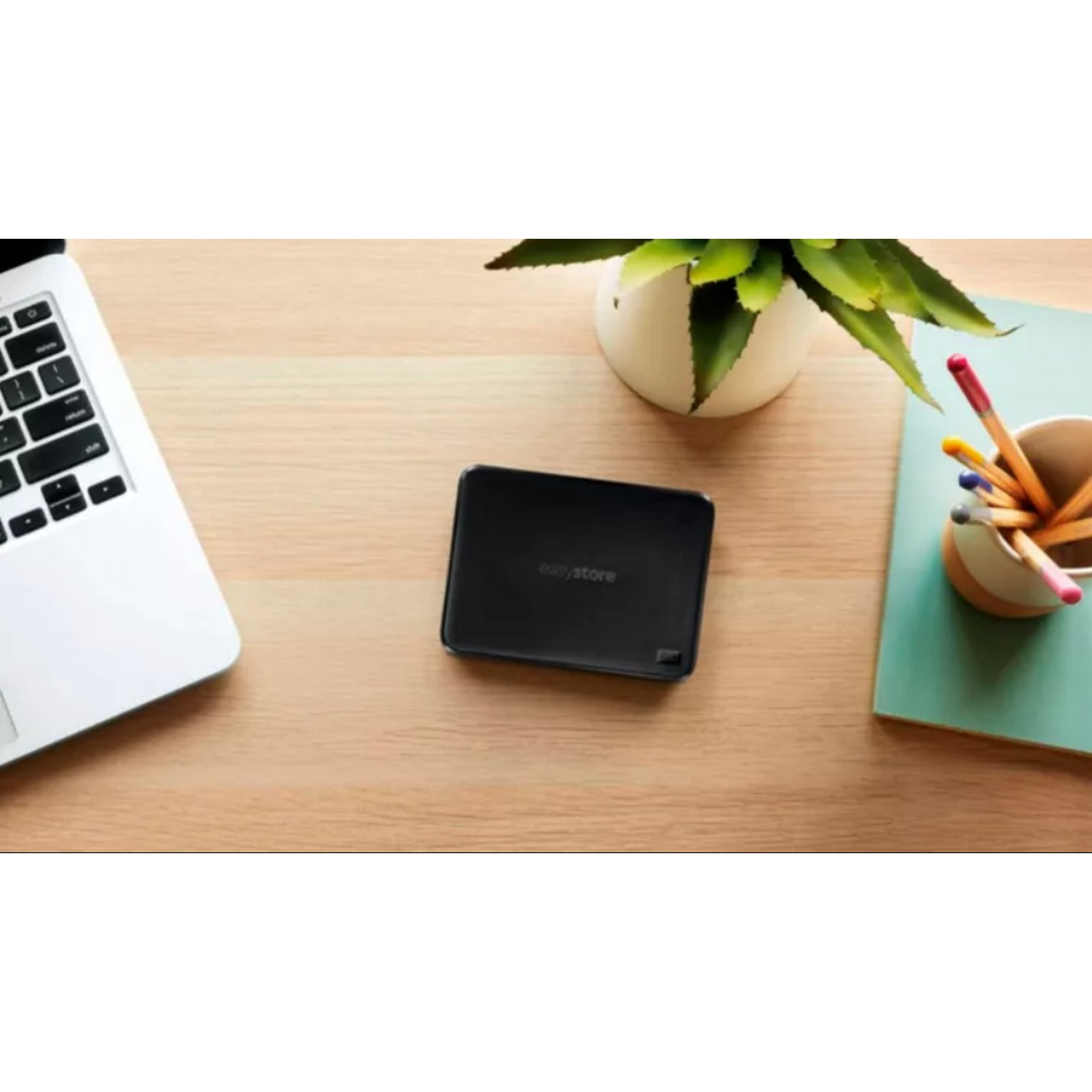 Disco duro externo negro sobre un escritorio de madera con una laptop, un portalápices y bolígrafos.