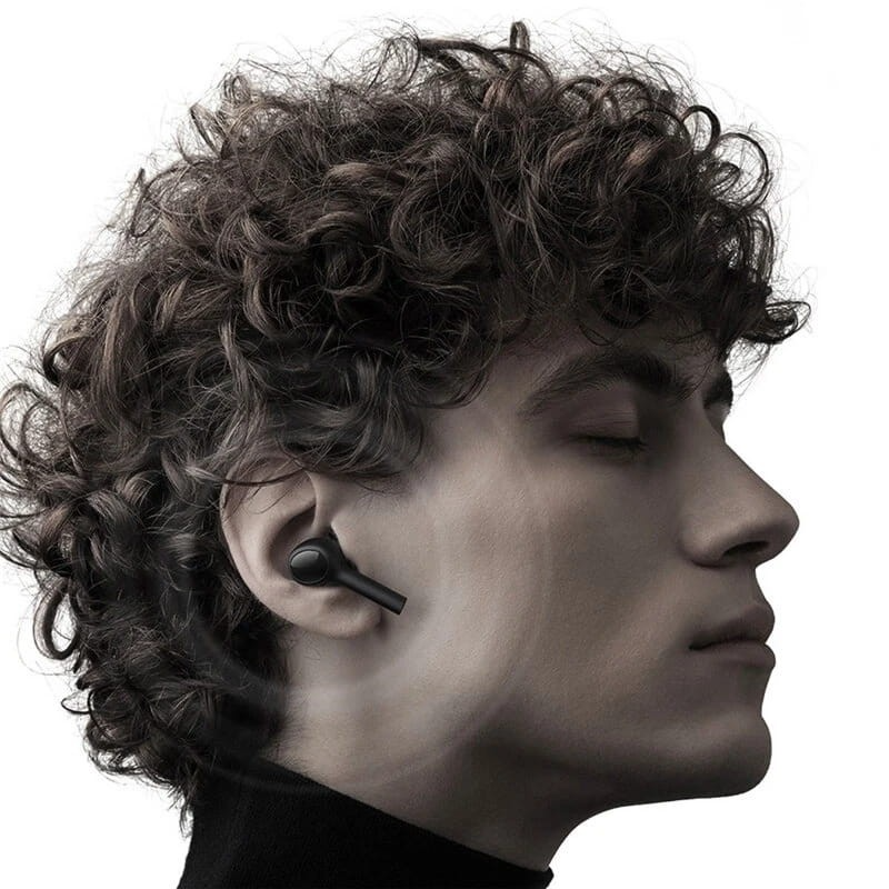 Un homme aux cheveux bouclés a un écouteur dans l'oreille. Il est de profil.