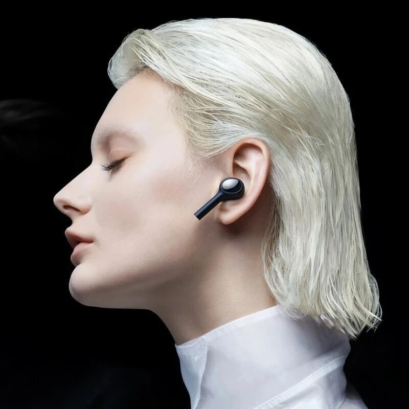 Femme aux cheveux blancs portant un écouteur noir. Vue de profil sur fond noir.