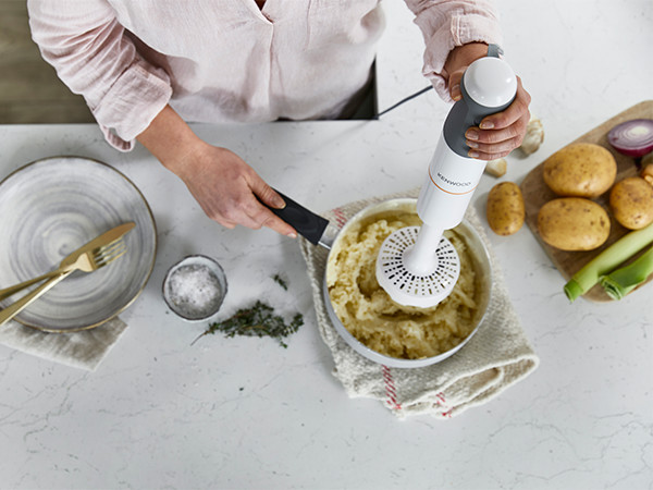 A woman blending mashed potatoes with a hand blender on a countertop.