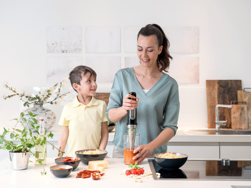 A woman and a boy preparing food in a kitchen with a blender and bowls of ingredients.