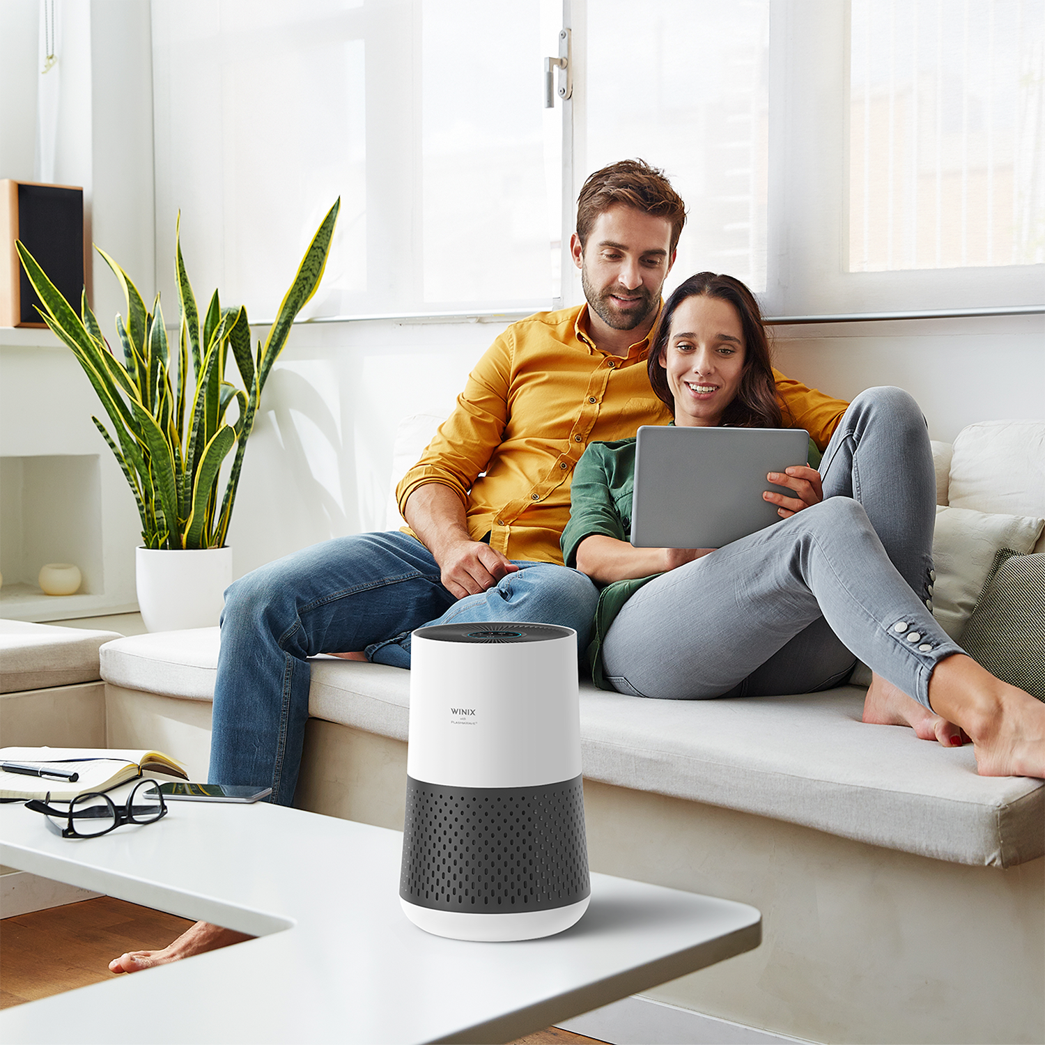 Couple on a couch with a tablet and an air purifier near a plant.