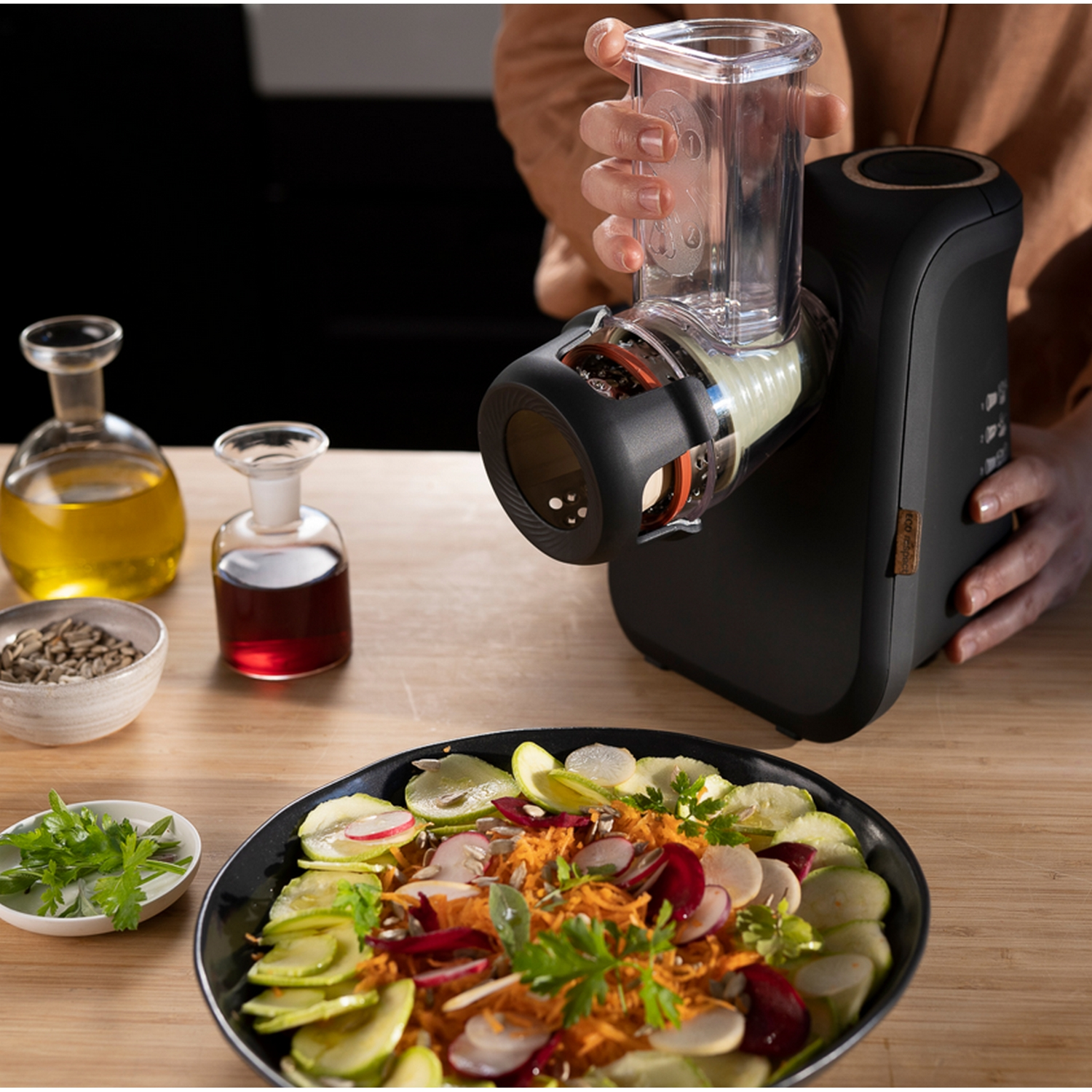 Una persona usando un cortador de verduras negro. En la mesa hay ensalada e ingredientes.