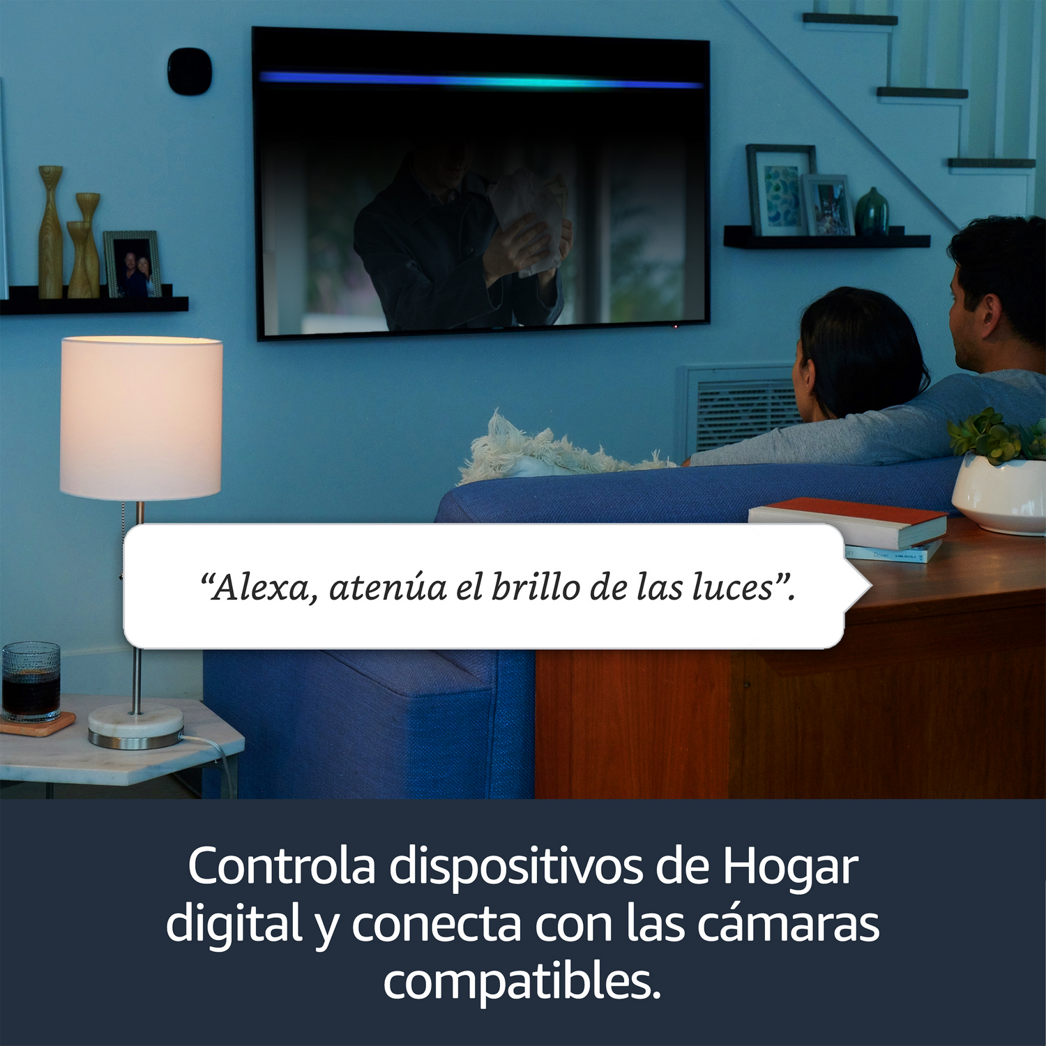 Una pareja ve la tele, una lámpara inteligente está encendida en primer plano. El texto dice: "Alexa, atenúa las luces".