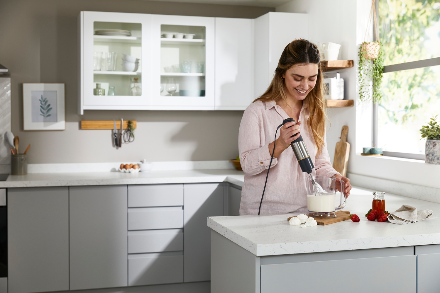 Frau in der Küche benutzt einen Stabmixer, rührt in einem Glas.