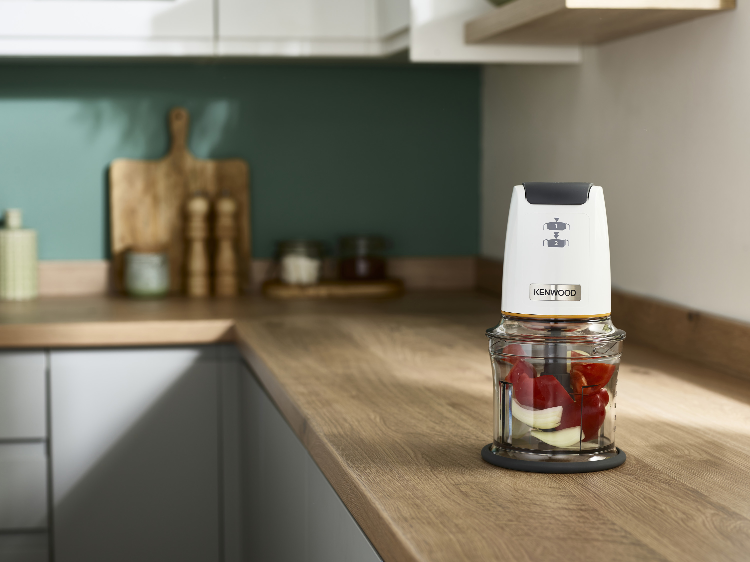 Ein Kenwood-Zerkleinerer mit gehacktem roten und weißen Gemüse auf einer Holztheke.