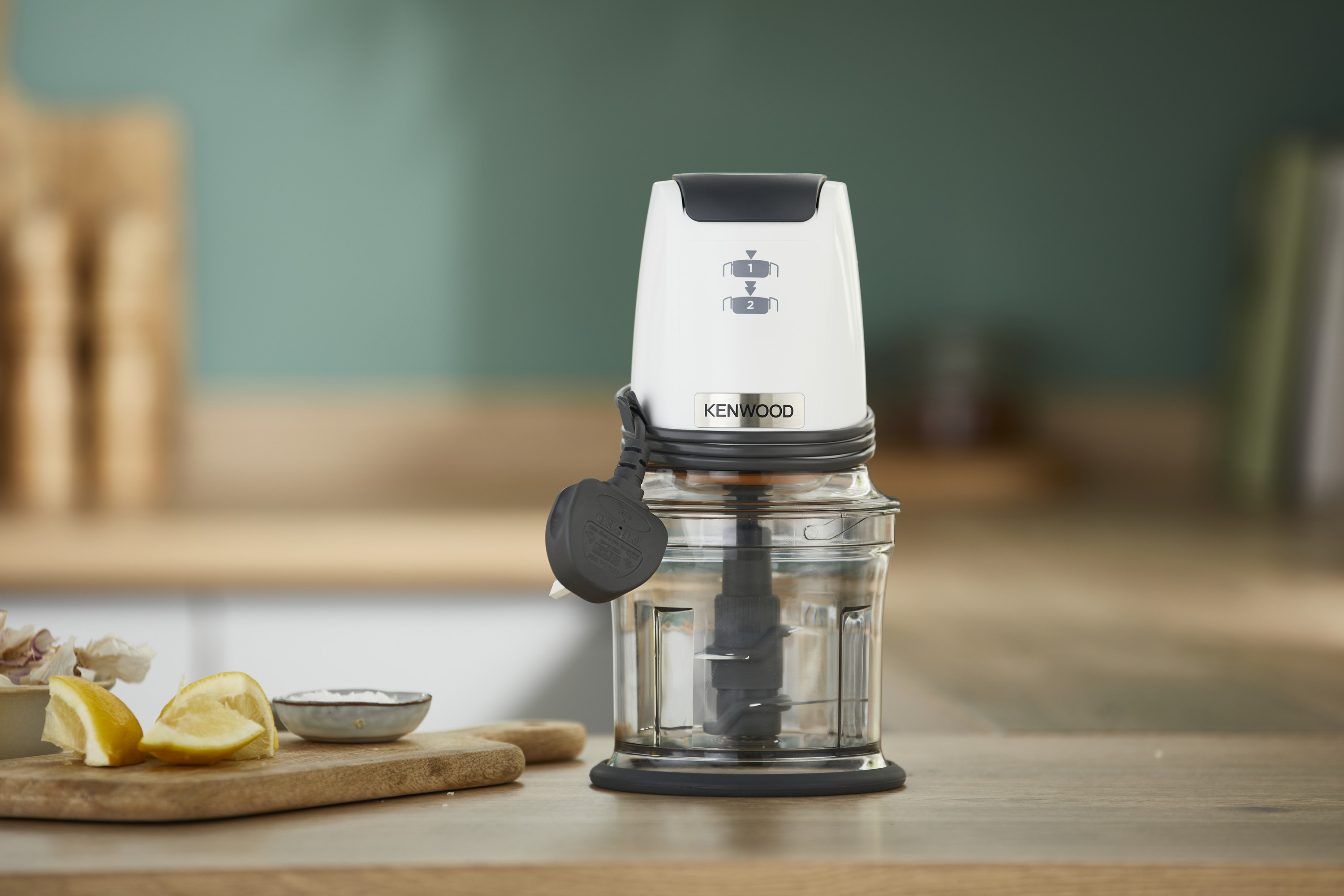 Ein Kenwood-Zerkleinerer auf einer Holztheke, mit Zitronen und Knoblauch im Vordergrund.