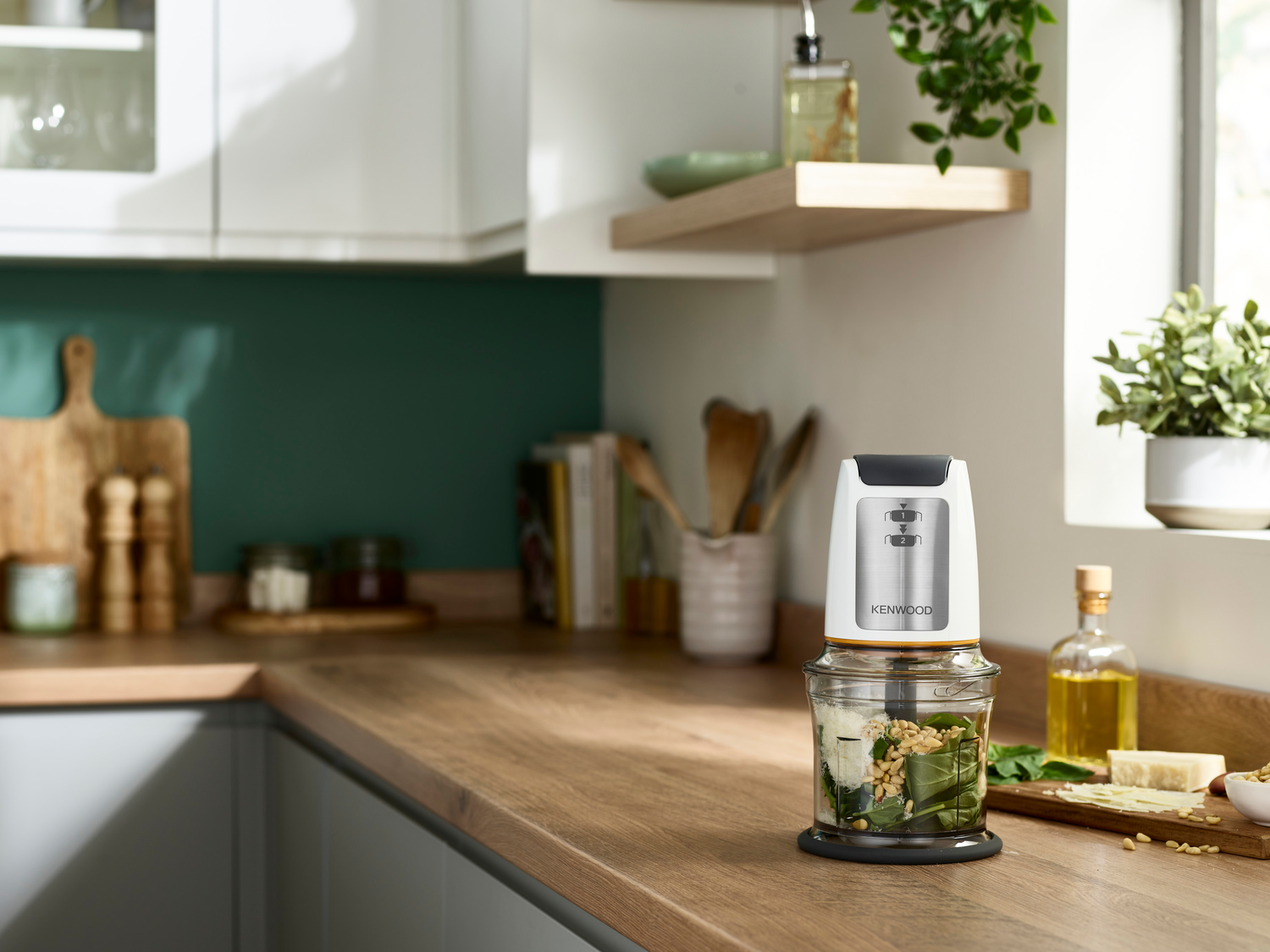 Weißer und silberner Kenwood-Foodprozessor auf einer Holztheke mit Zutaten.