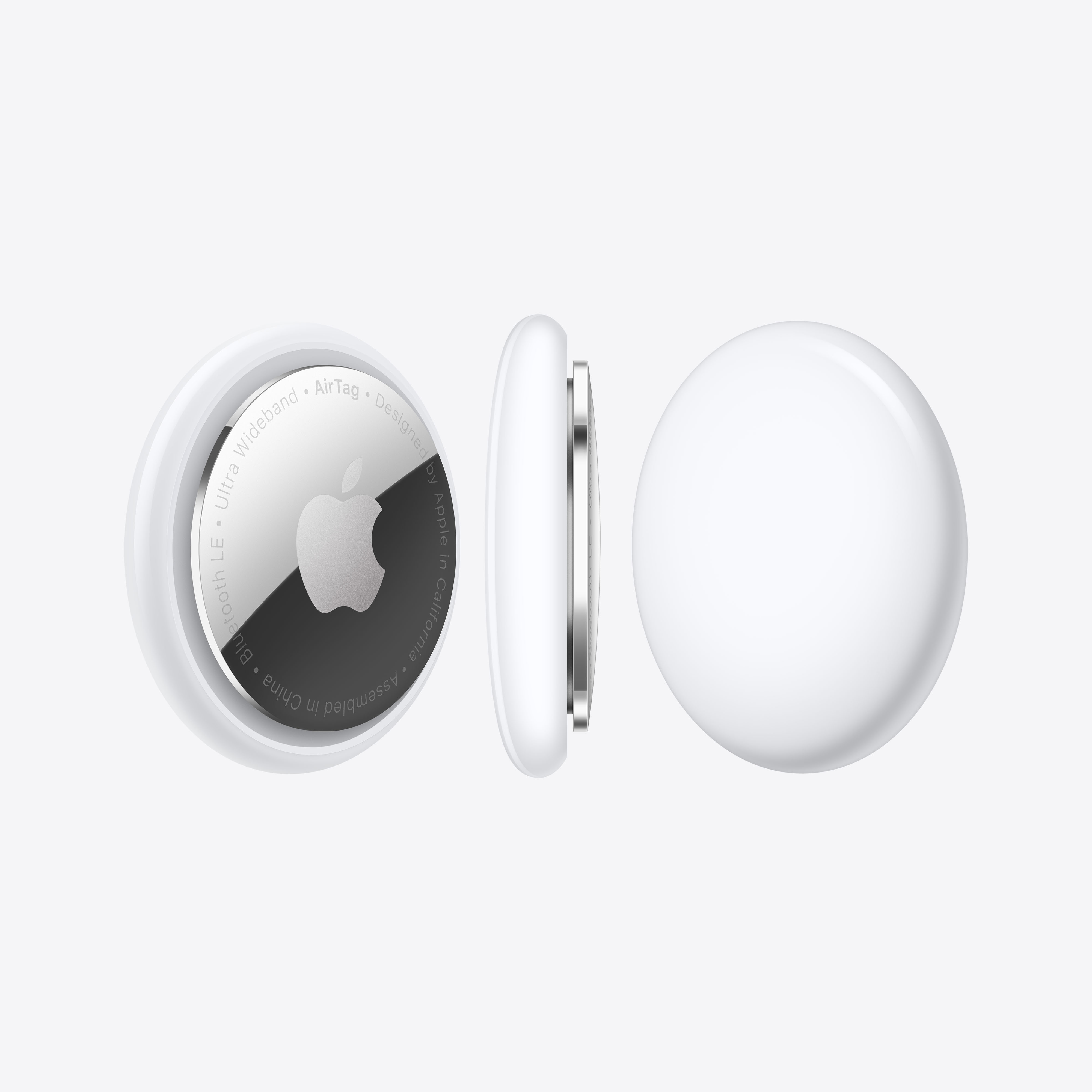 Tres AirTags blancos de Apple. Uno muestra el logotipo de Apple. Están sobre una superficie blanca.