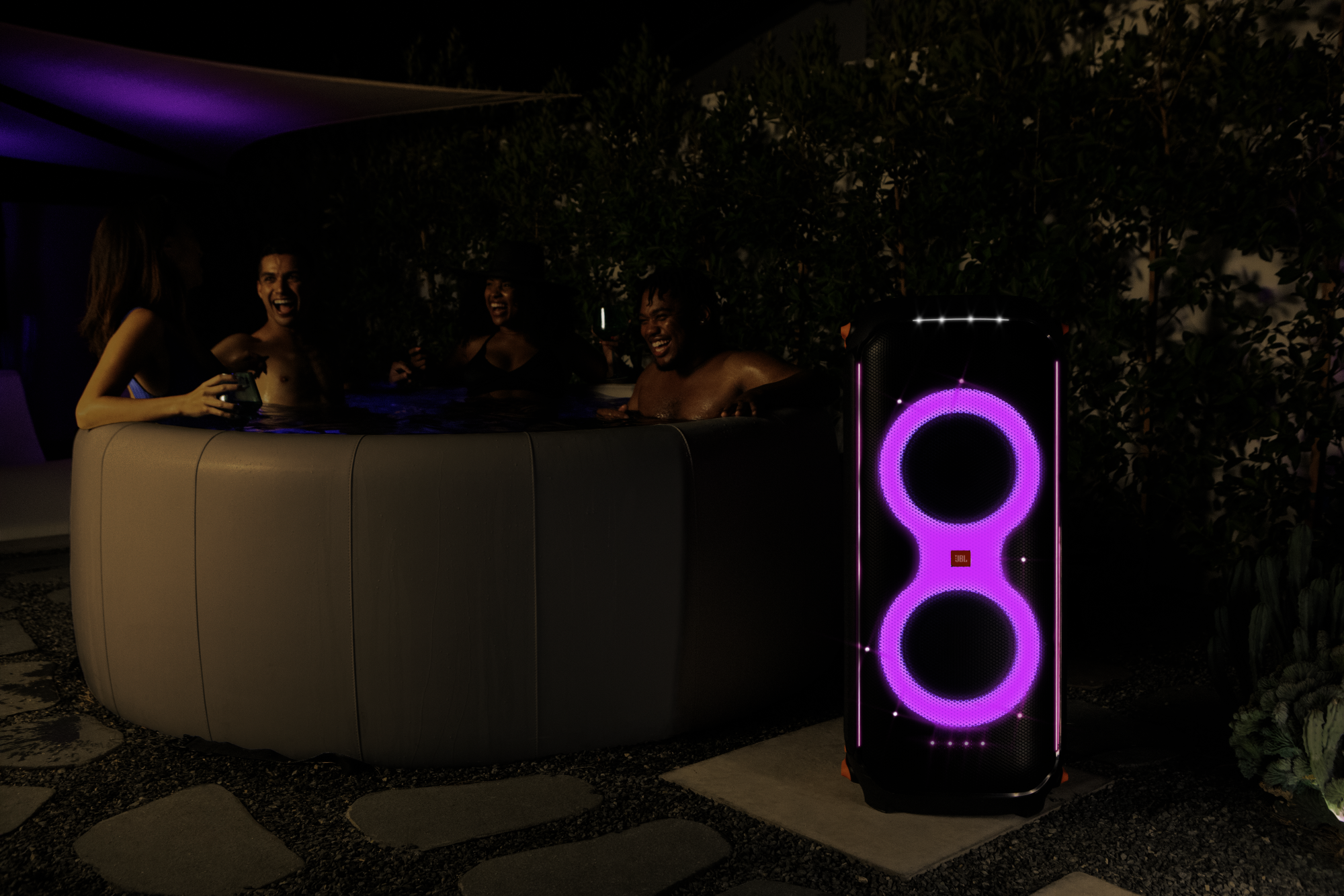 Des gens dans un jacuzzi avec une enceinte de fête, éclairée de lumières roses.