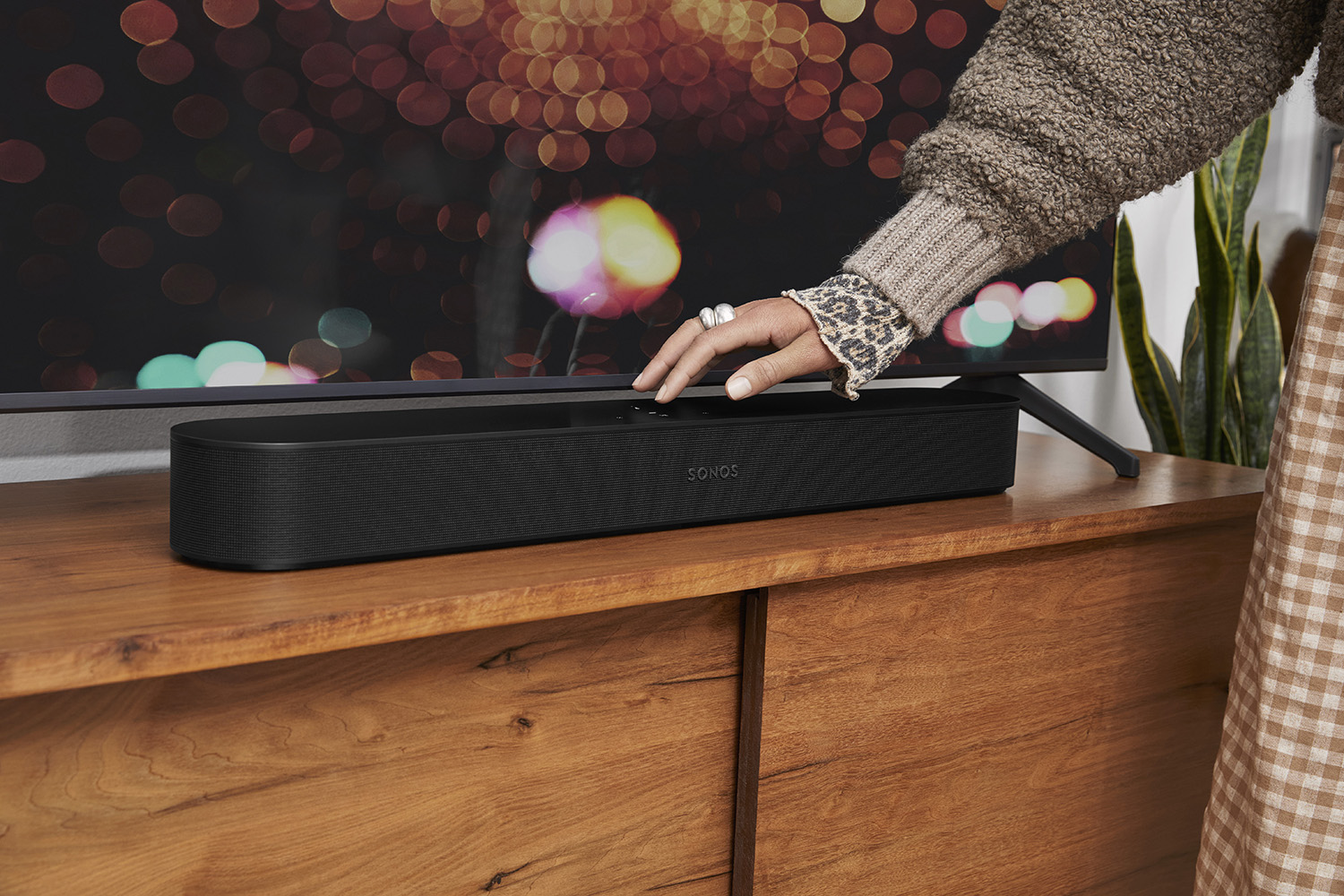 Hand van persoon raakt zwarte Sonos soundbar aan op houten kast.