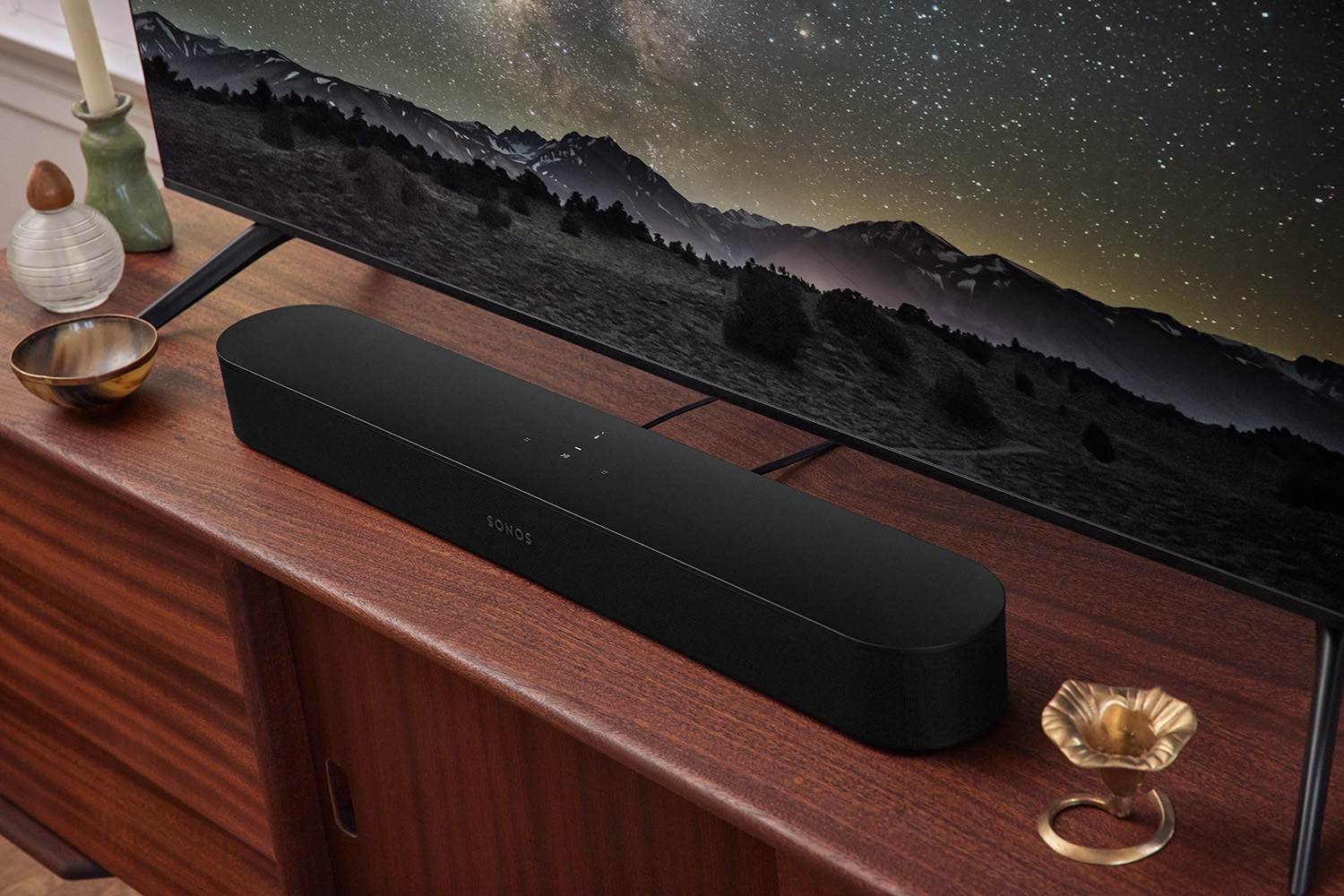 Zwarte Sonos soundbar op een houten kast, met een tv-scherm op de achtergrond.