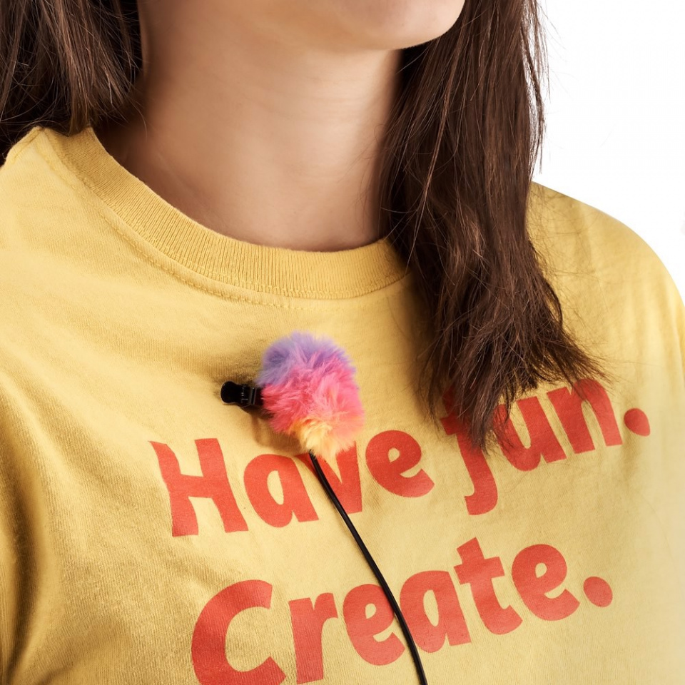 Une femme avec un micro coloré sur son t-shirt qui dit : 'Have fun. Create'.