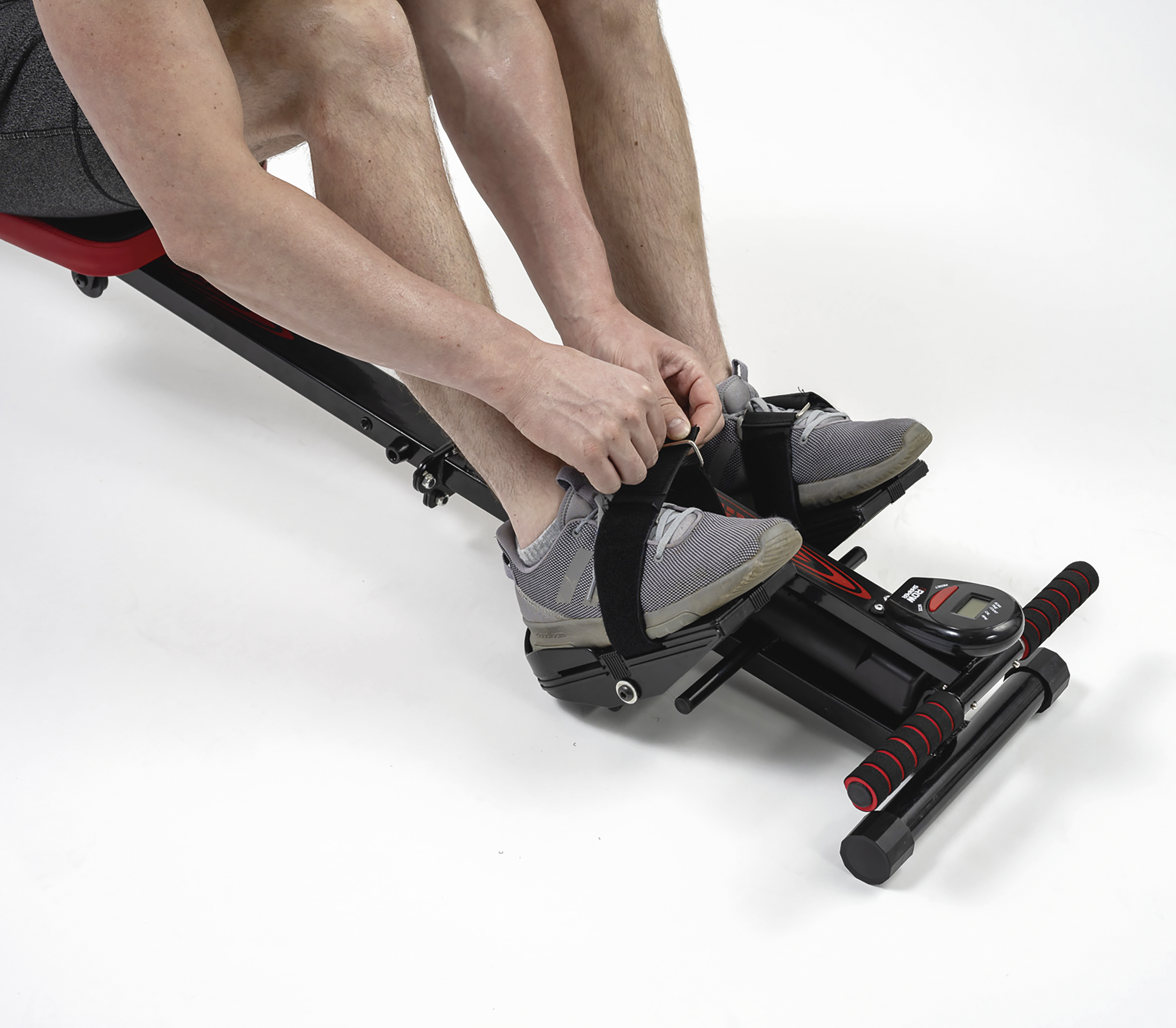 Die Füße einer Person in grauen Turnschuhen sind in einer Rudermaschine befestigt.