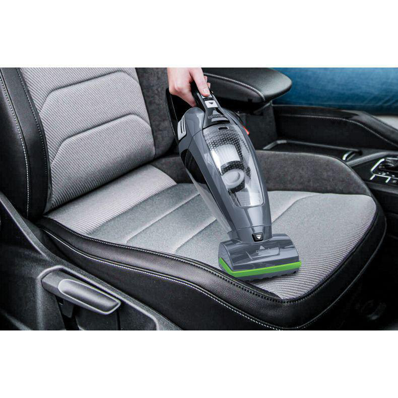 Eine Hand hält einen grau-schwarzen Handstaubsauger über einem Autositz.