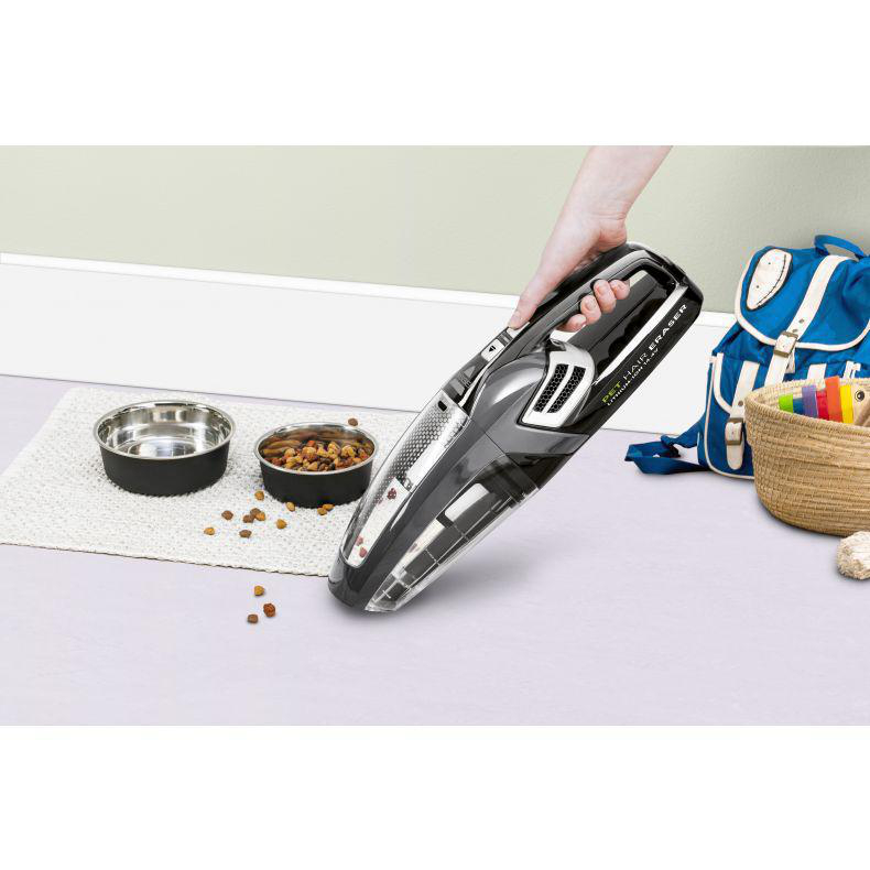 Hand hält Staubsauger. Schalen und Tasche im Hintergrund.