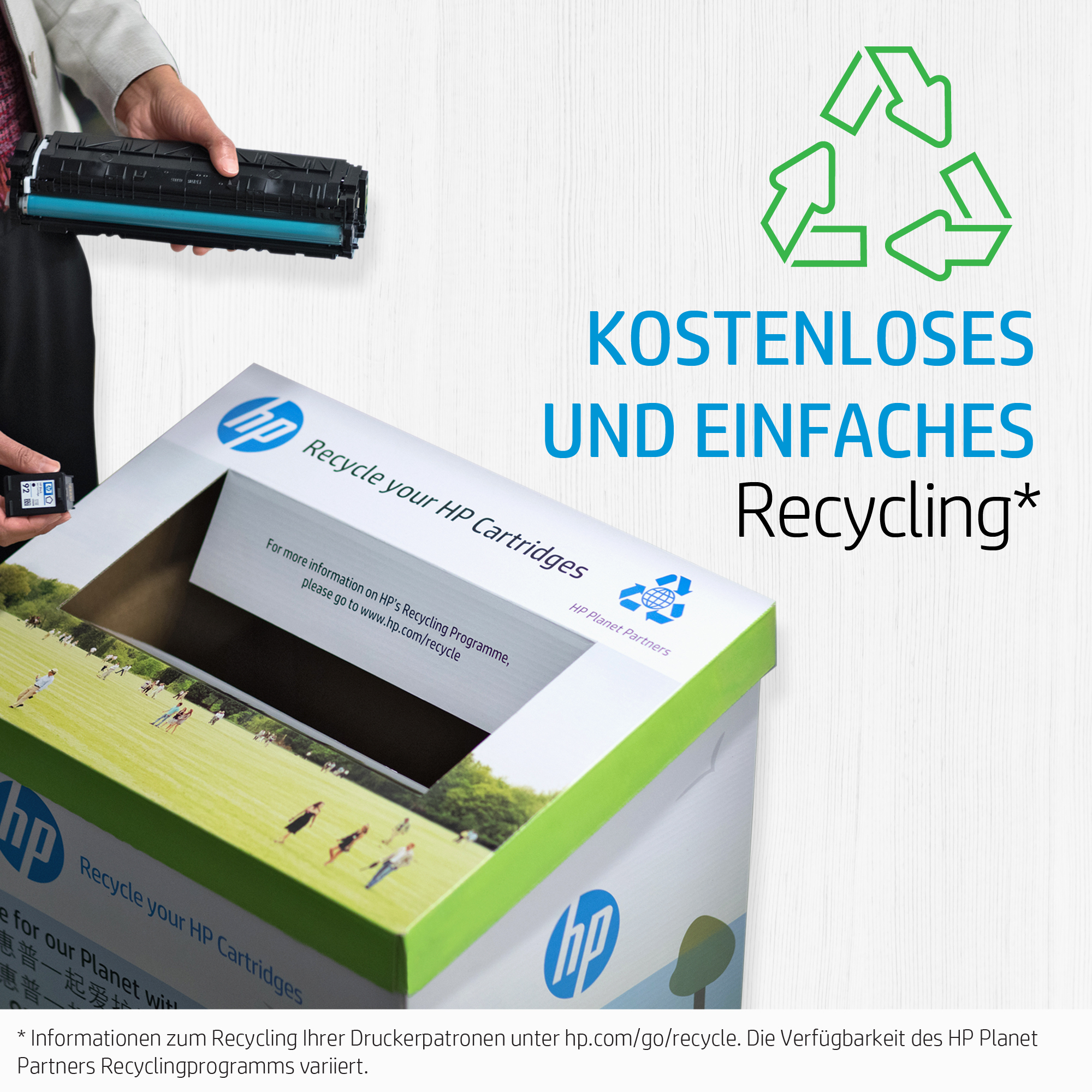 Person hält eine schwarze und türkisfarbene Tonerkartusche neben einer Recyclingtonne mit Text.