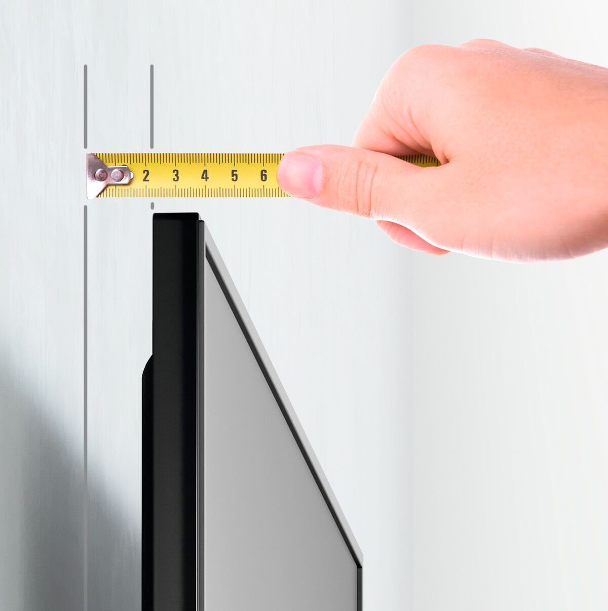 Hand holding a yellow tape measure near a wall, measuring distance.