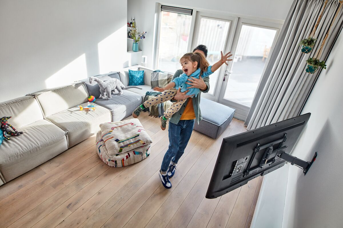 Een man houdt een kind vast in een woonkamer met een tv aan de muur.