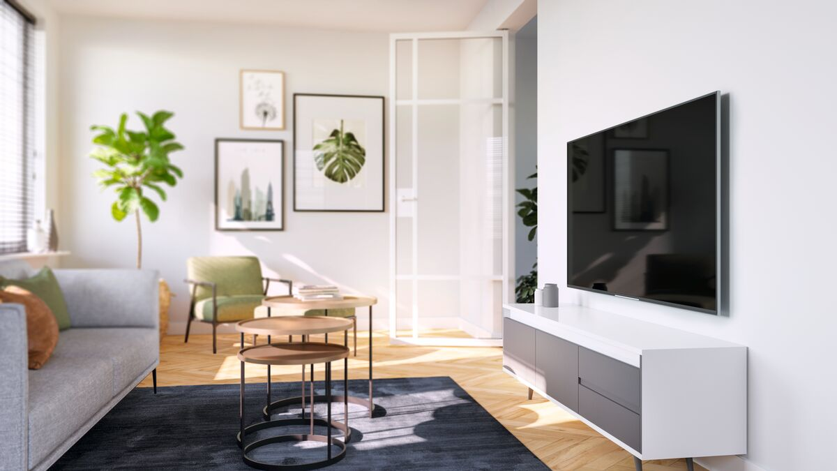 Living room scene. Grey sofa, side tables, framed art, and a mounted TV.