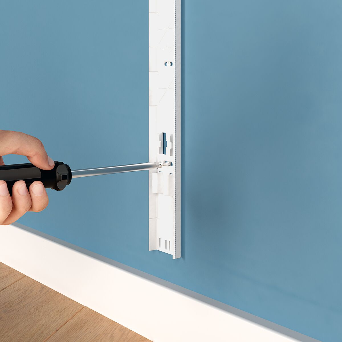 A hand using a screwdriver to fasten a white bracket to a blue wall. The bracket is for wall mounting.