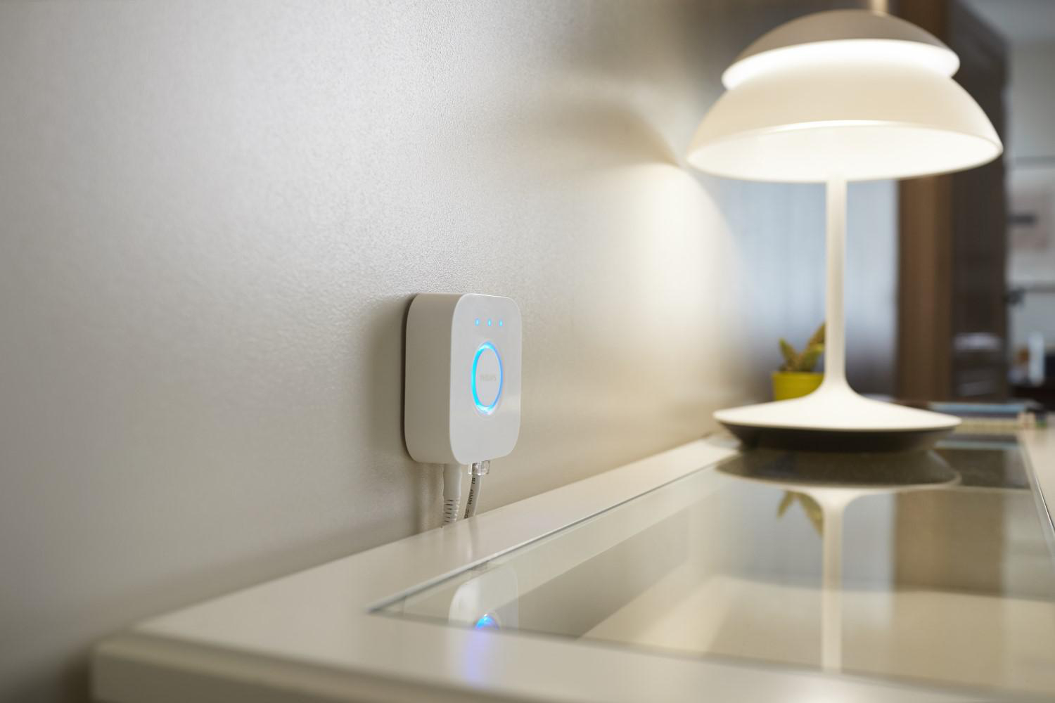Weißes Smart Home-Hub an einer Wand mit einer Lampe in der Nähe.