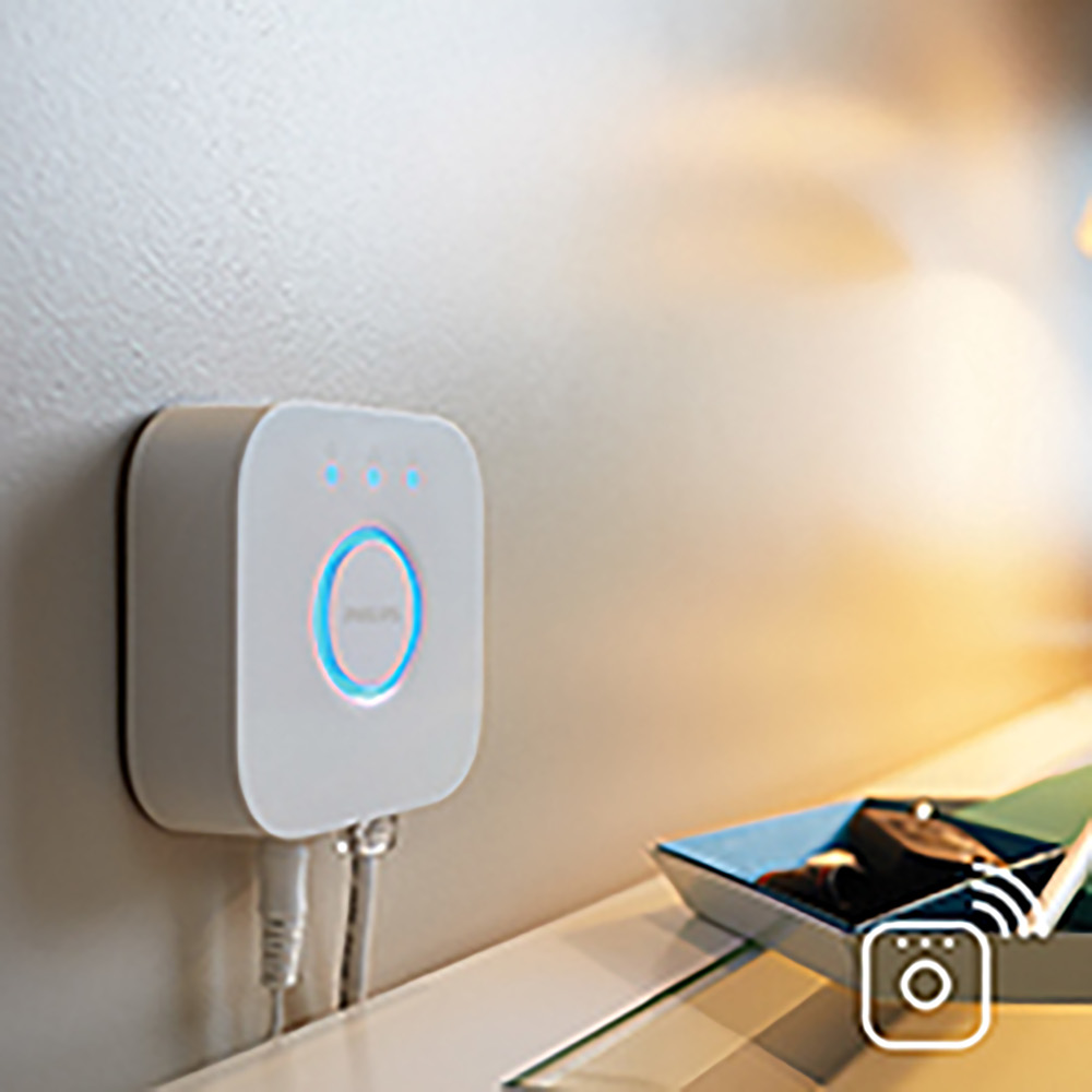 White smart home hub, glowing, mounted on a wall, near a small decorative tray.