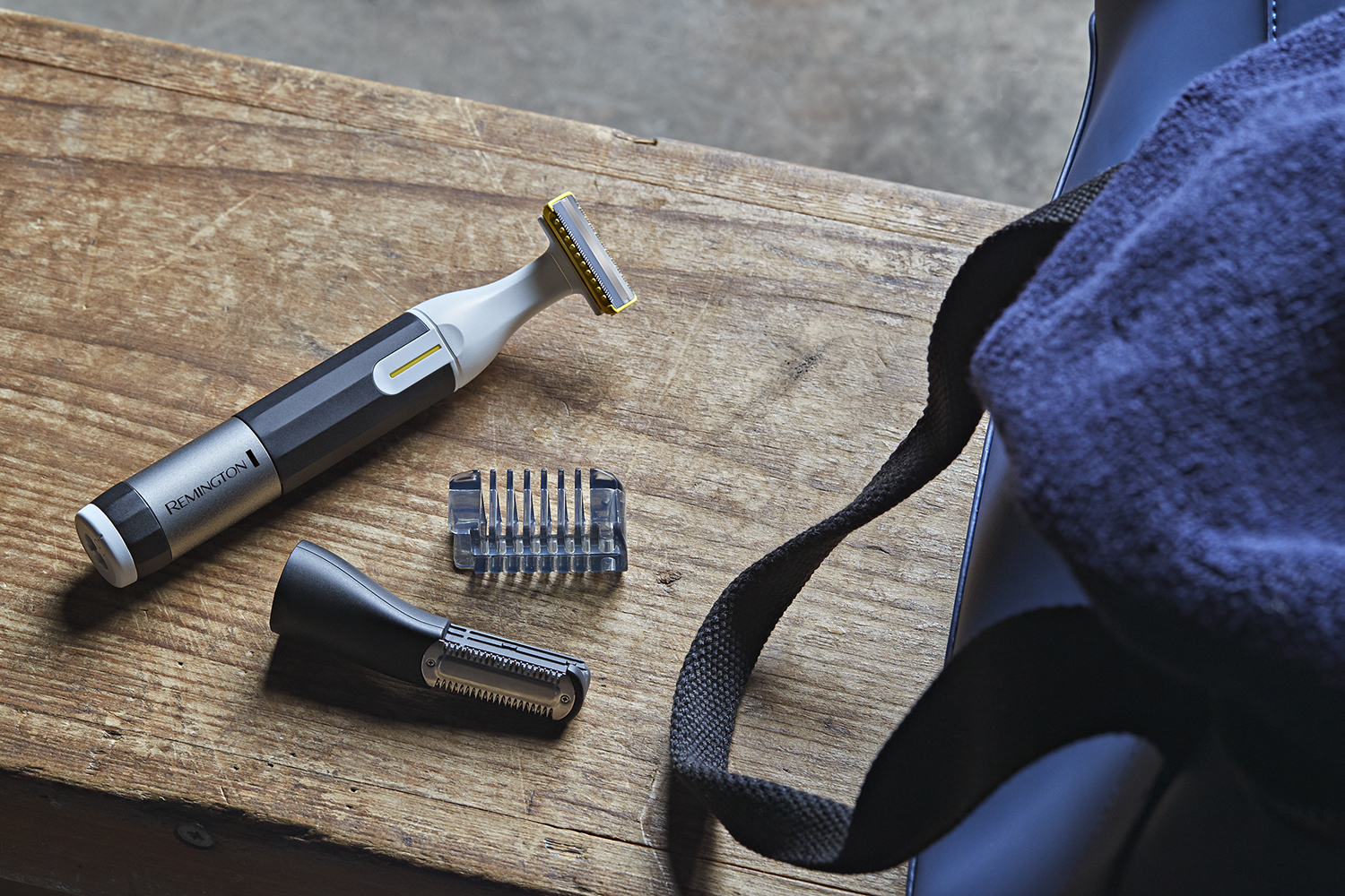 A razor with accessories sits on wood, a blue bag is in the background.