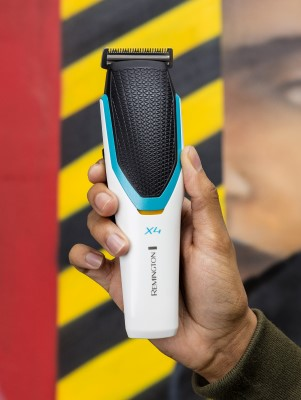A person holding a white, black, and teal electric beard trimmer. Background features a yellow and black wall.