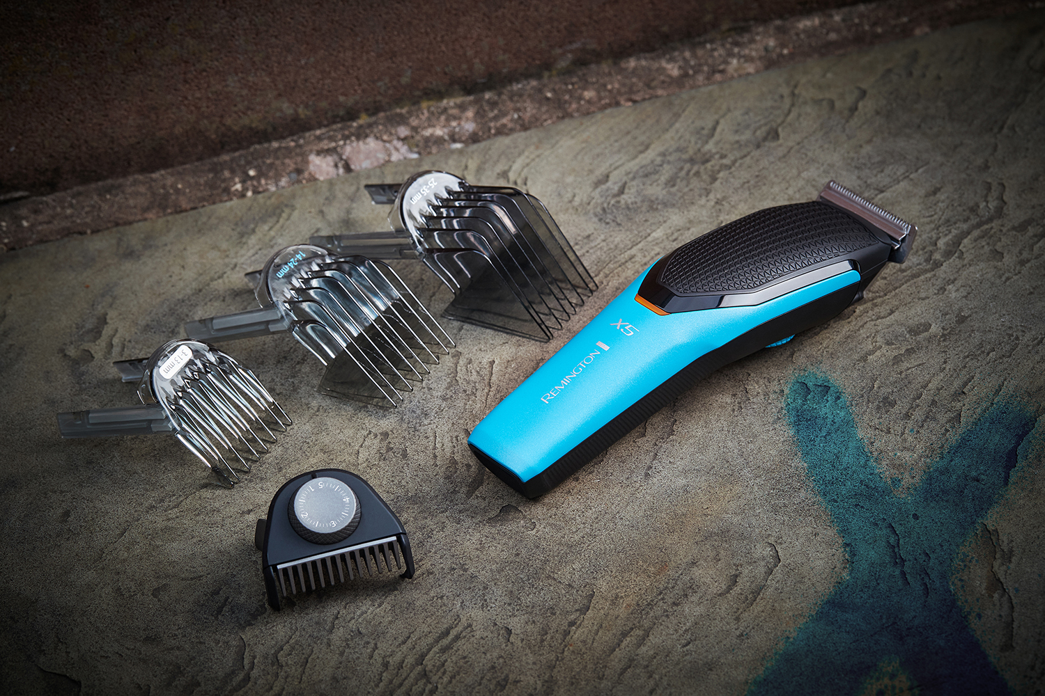 Remington hair clipper, blue, with attachments on a stone surface.
