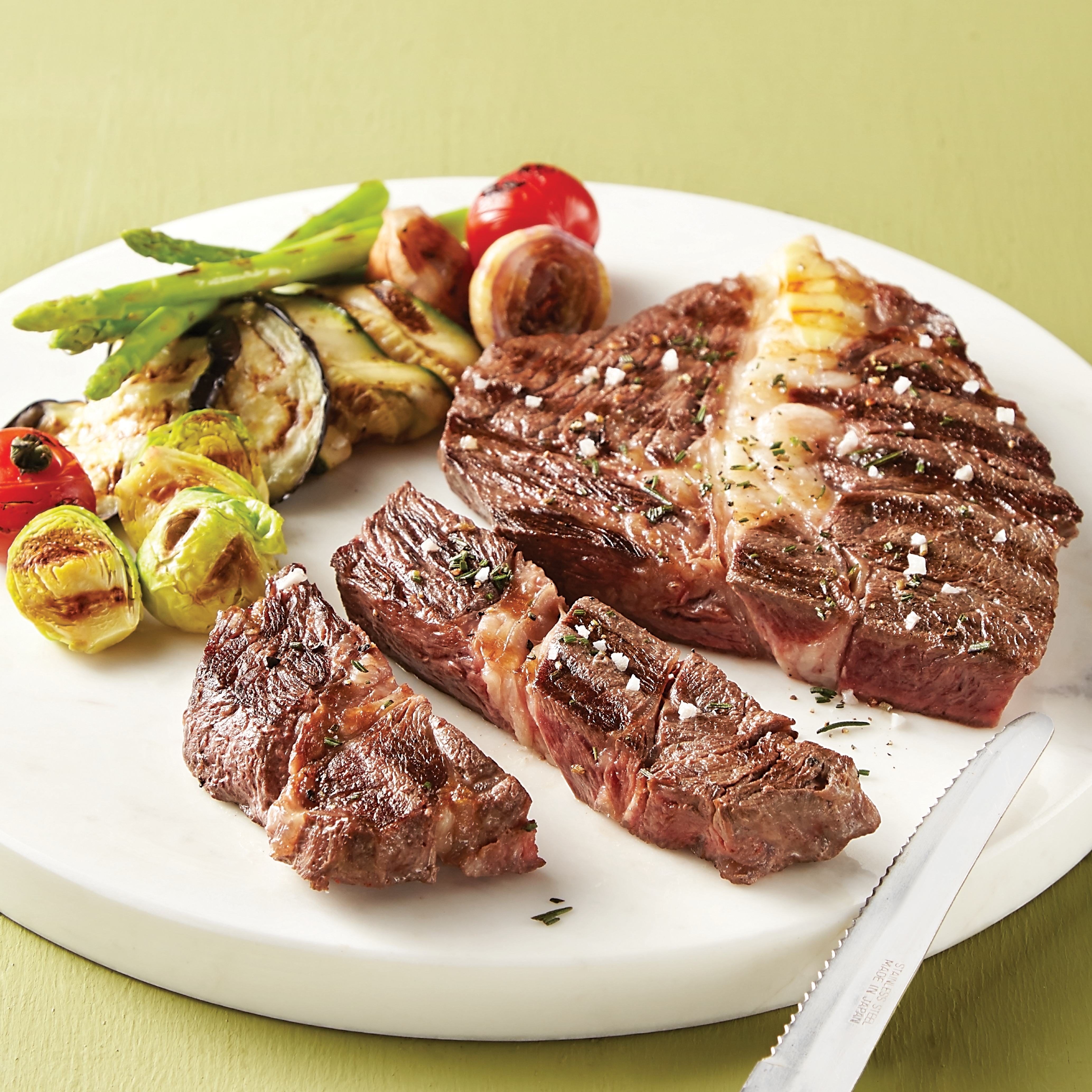 Grillezett steak zöldségekkel fehér tányéron. Spárga, paradicsom és cukkini.