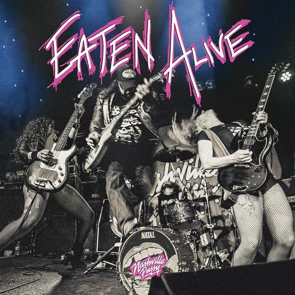 Band op het podium: Eaten Alive banner, muzikanten spelen instrumenten, drumstel, lichten.